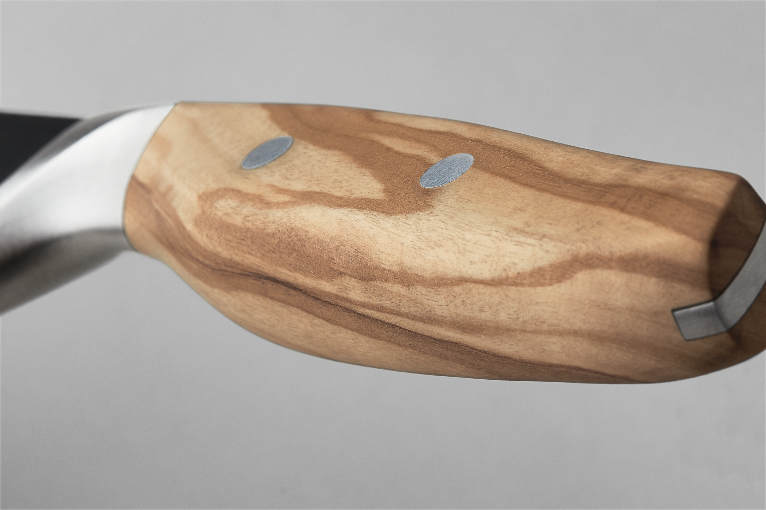 Primer plano del mango de un cuchillo. Es de madera, tiene detalles metálicos y sobre un fondo gris.
