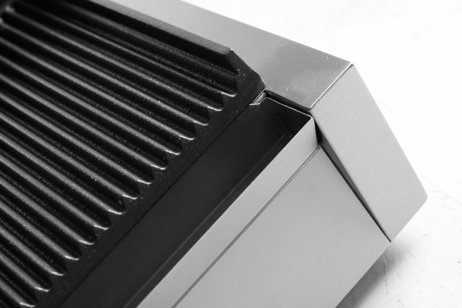Nahaufnahme eines metallischen schwarzen Grills mit Rillen, Teil eines Sandwichmakers. Weißer Hintergrund.