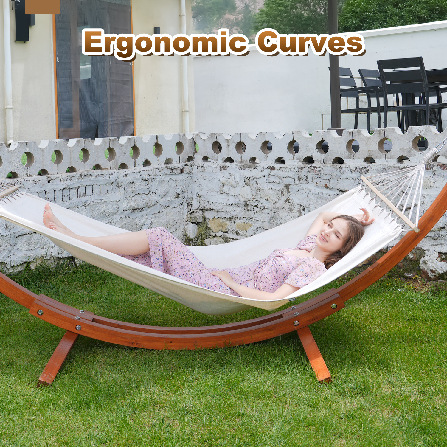 Kobieta relaksująca się w hamaku na zielonym trawniku, z kamiennym murem w tle. Tekst brzmi: Ergonomiczne krzywizny.
