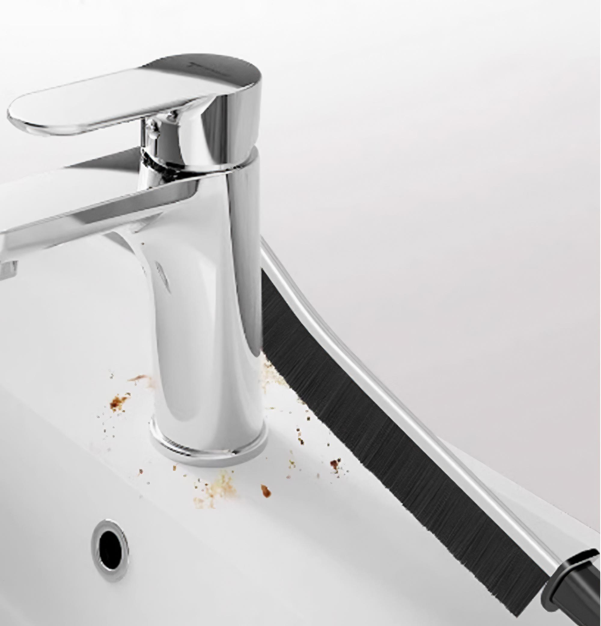 Ein Chromhahn über einem weißen Waschbecken mit einer Reinigungsbürste. Braune Flecken sind auf dem Waschbecken sichtbar.