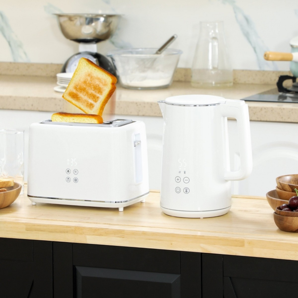 Weißer Toaster mit zwei herausspringenden Toastscheiben und ein weißer Wasserkocher auf einer Holztheke, mit anderen Gegenständen.