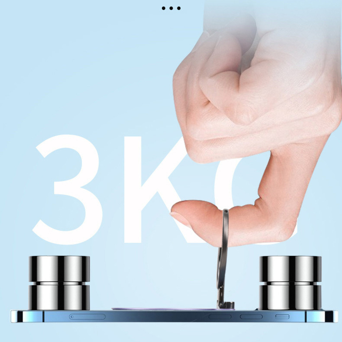 Dłoń trzyma pierścień, który jest przymocowany do telefonu. Telefon leży na niebieskiej powierzchni ze srebrnymi podstawkami.