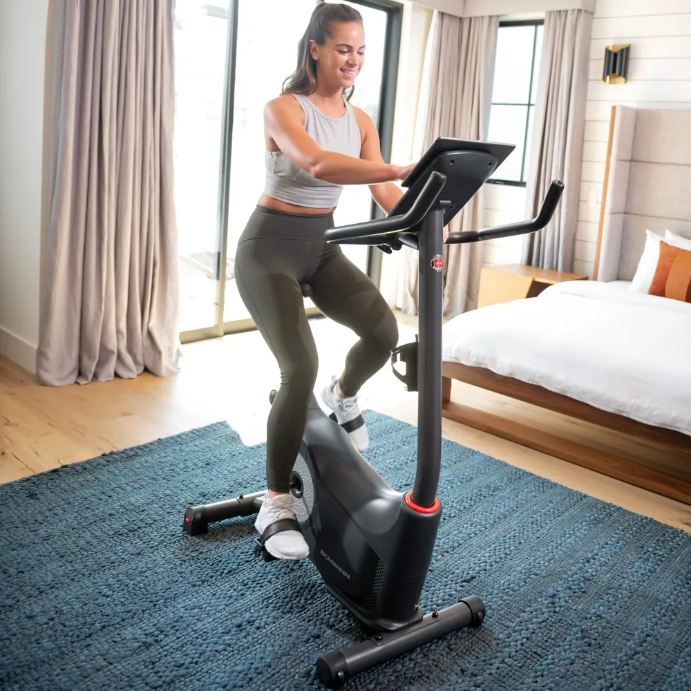 Une femme fait du vélo d'appartement dans une pièce avec un lit et une fenêtre.
