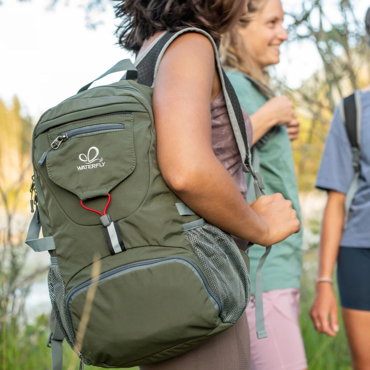 Una persona usando una mochila Waterfly verde. Otras dos personas están borrosas en el fondo.