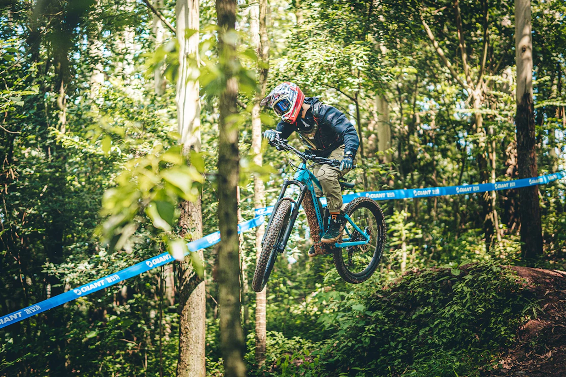 Ein Biker springt mit einem blauen Mountainbike bei einem Wettbewerb in einem Wald.