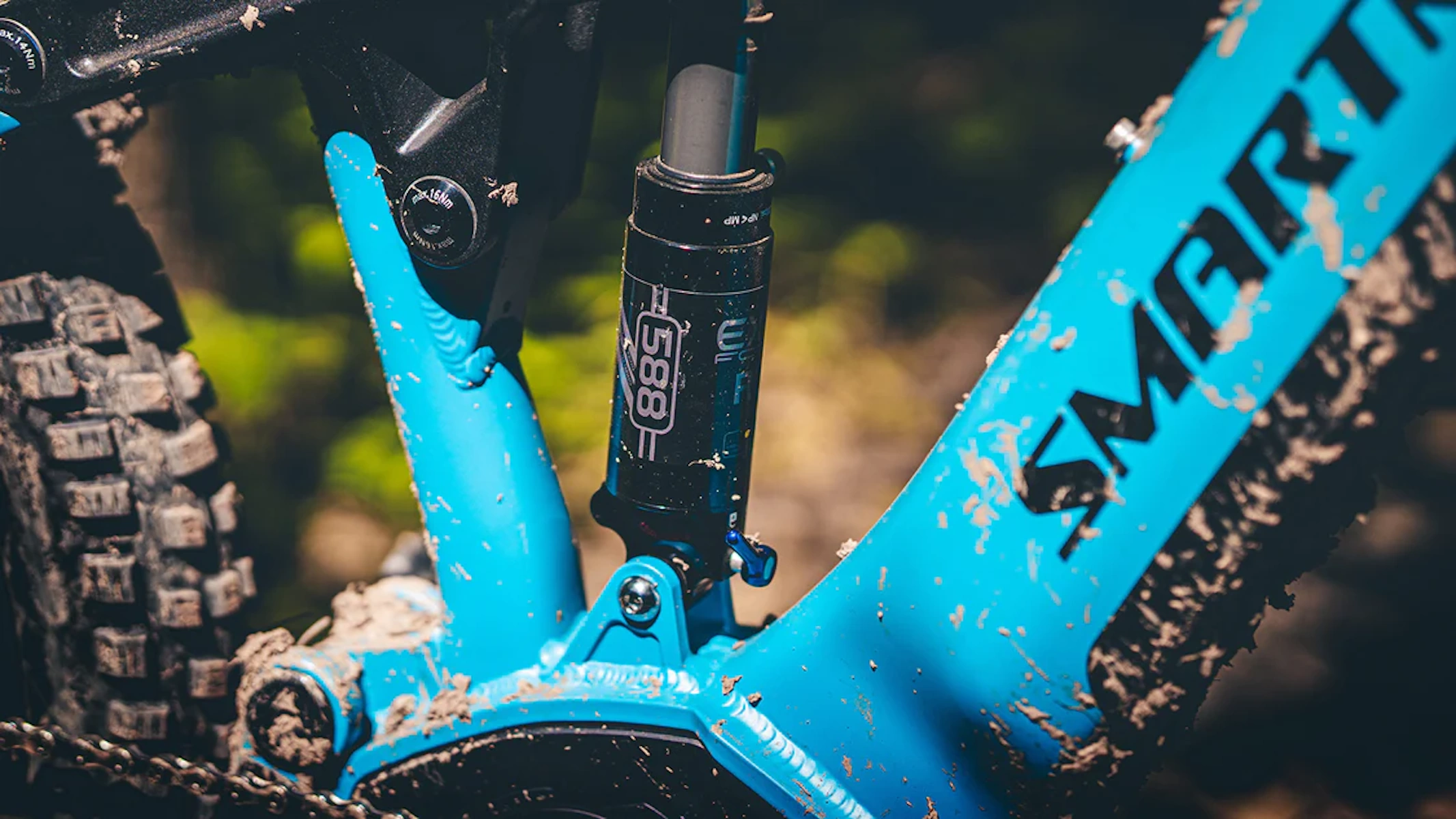Nahaufnahme eines blauen Mountainbike-Rahmens mit Smartmotion-Logo. Schlamm und Federungsteile sichtbar.