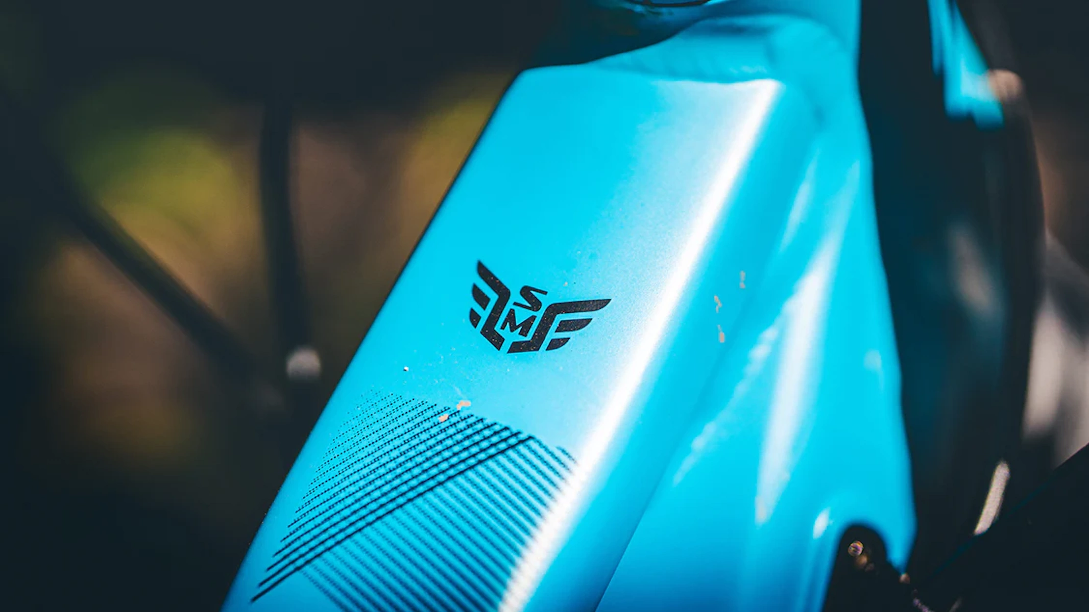Nahaufnahme des blauen Fahrradrahmens mit Logo. Das Logo hat Flügel und die Buchstaben SMS.