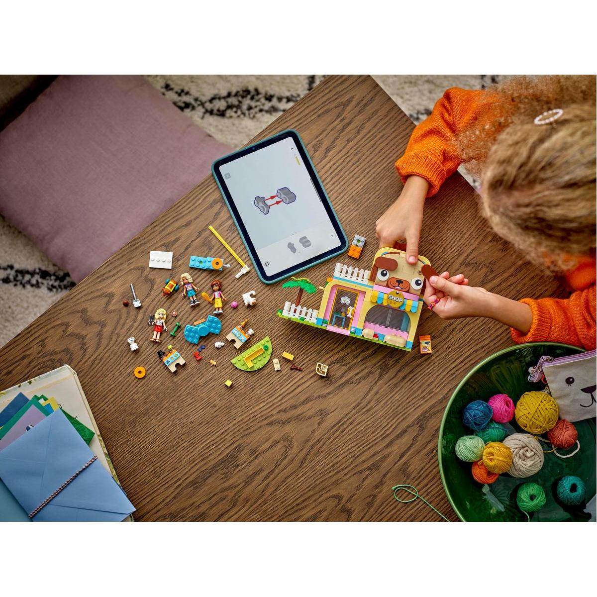 Osoba buduje zestaw Lego sklepu w kształcie psa. Na drewnianym stole są rozrzucone elementy.