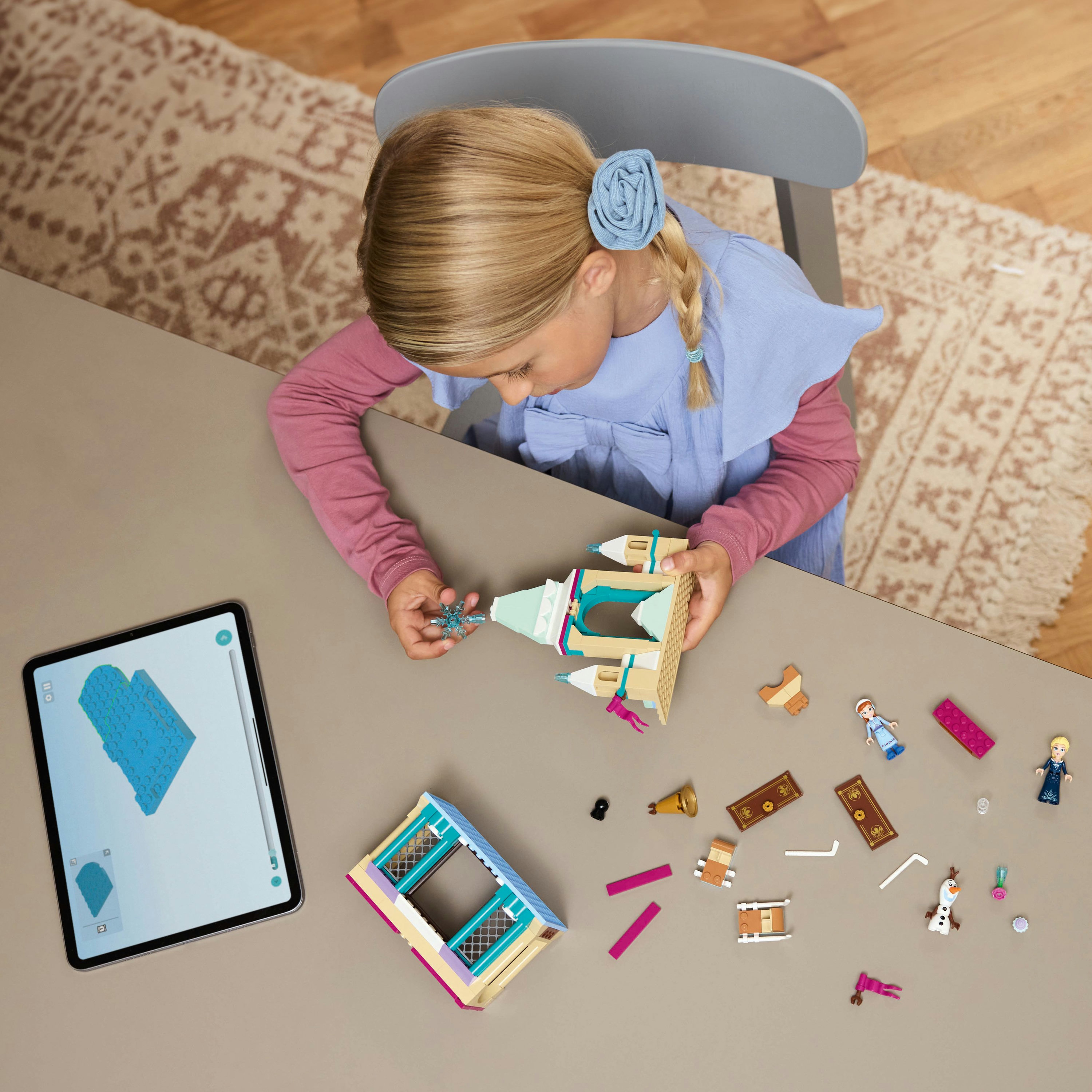 Dziewczynka buduje zamek Lego. Na stole są klocki Lego i tablet z instrukcjami. W tle dywan.