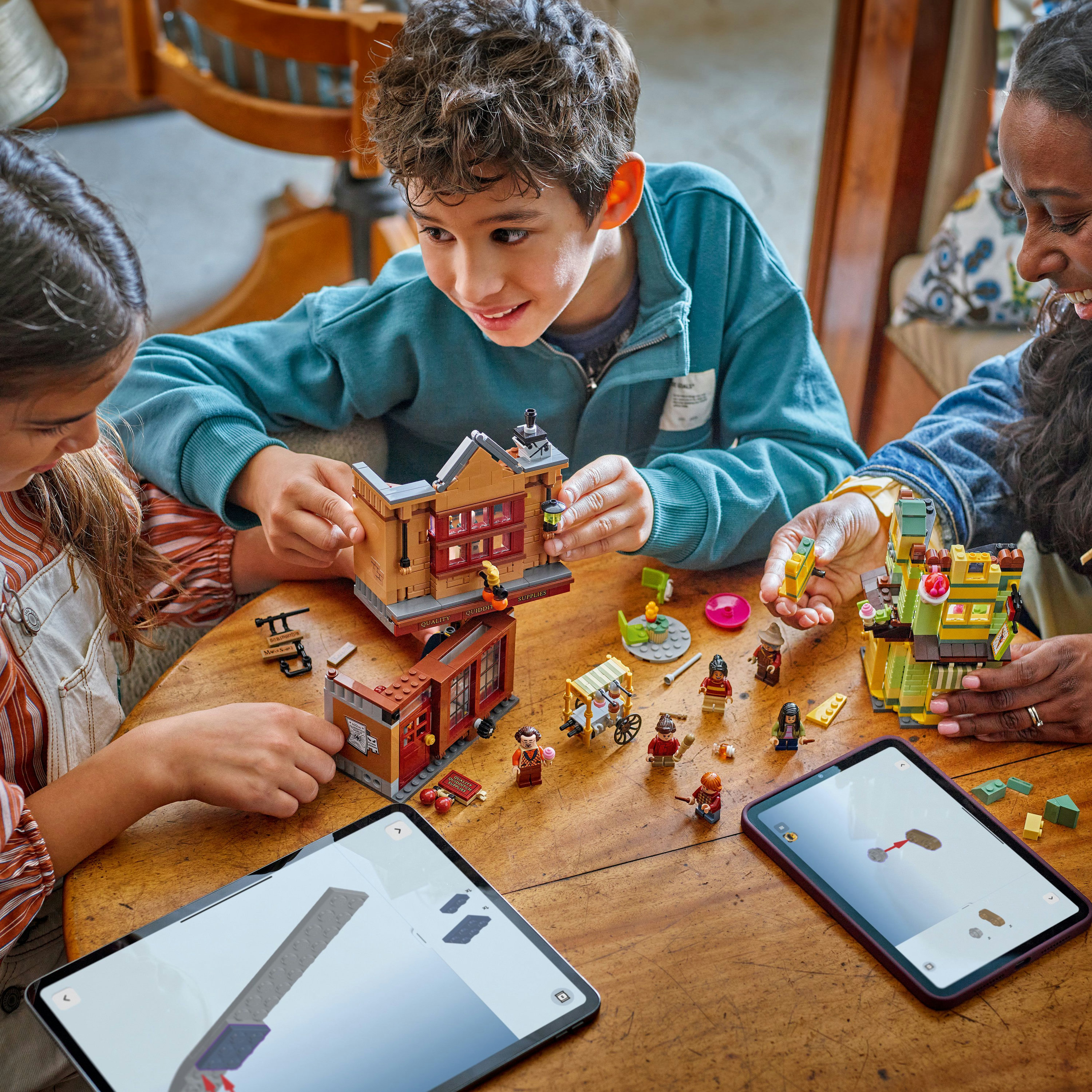Troje dzieci buduje konstrukcje z Lego na drewnianym stole. Na stole są również tablety.