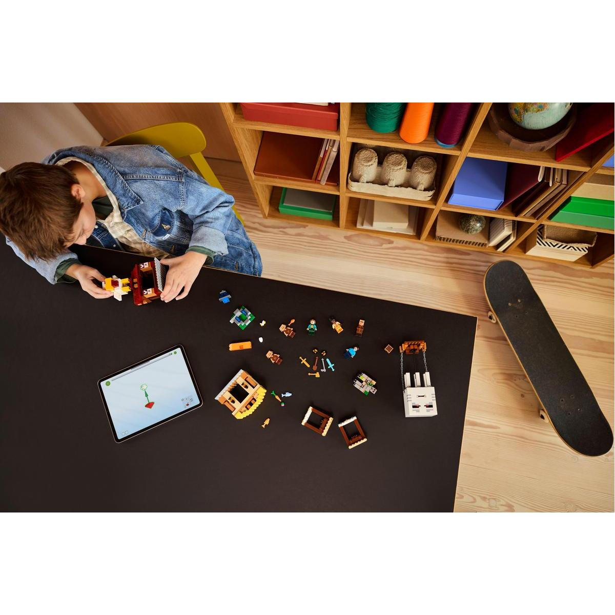Chłopiec buduje zestaw Lego. Na stole są klocki Lego i tablet z instrukcjami. W pobliżu deskorolka.