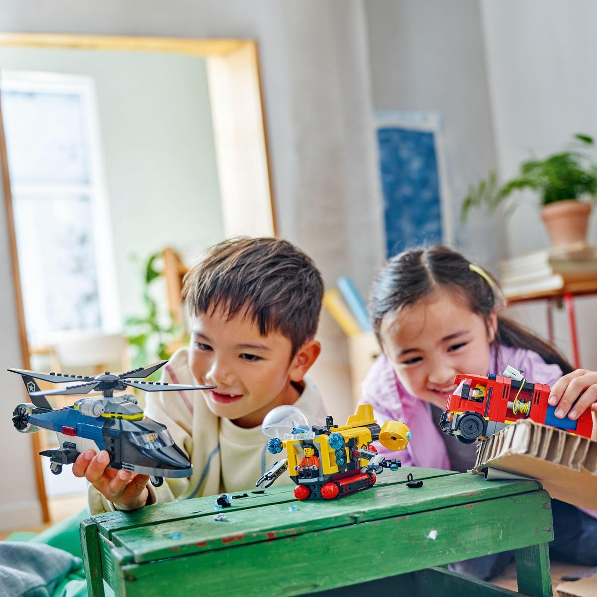 Dwoje dzieci bawi się modelami Lego helikoptera, łodzi podwodnej i wozu strażackiego.