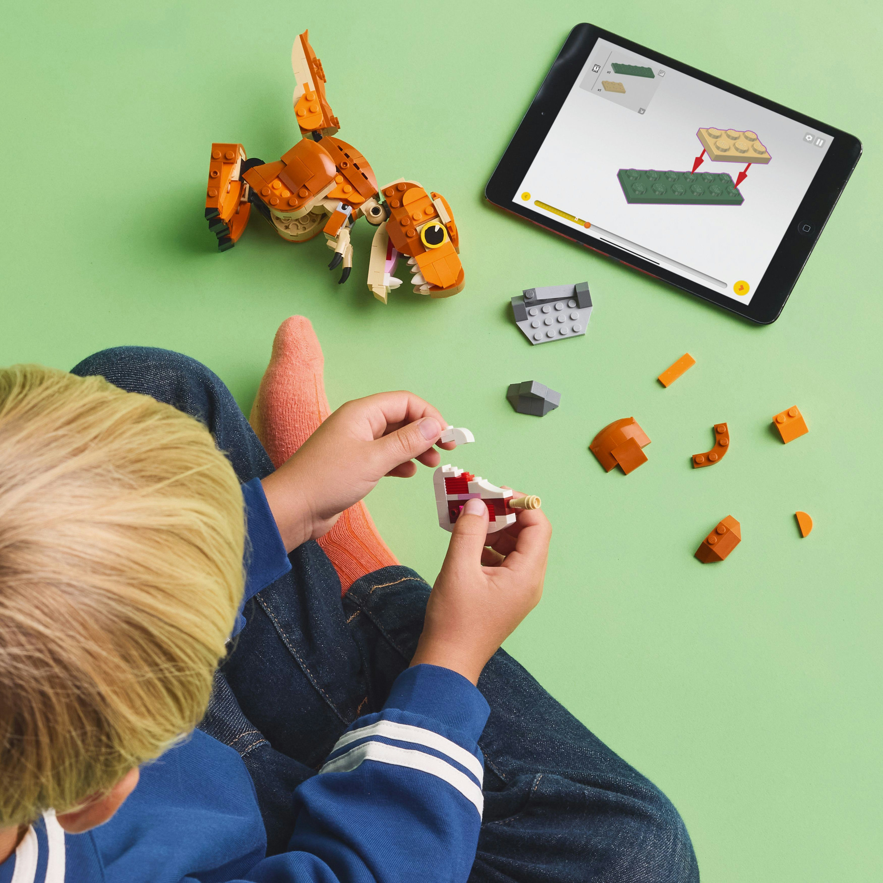 Dziecko buduje dinozaura Lego. Tablet pokazuje instrukcje. Obecne są różne elementy Lego.