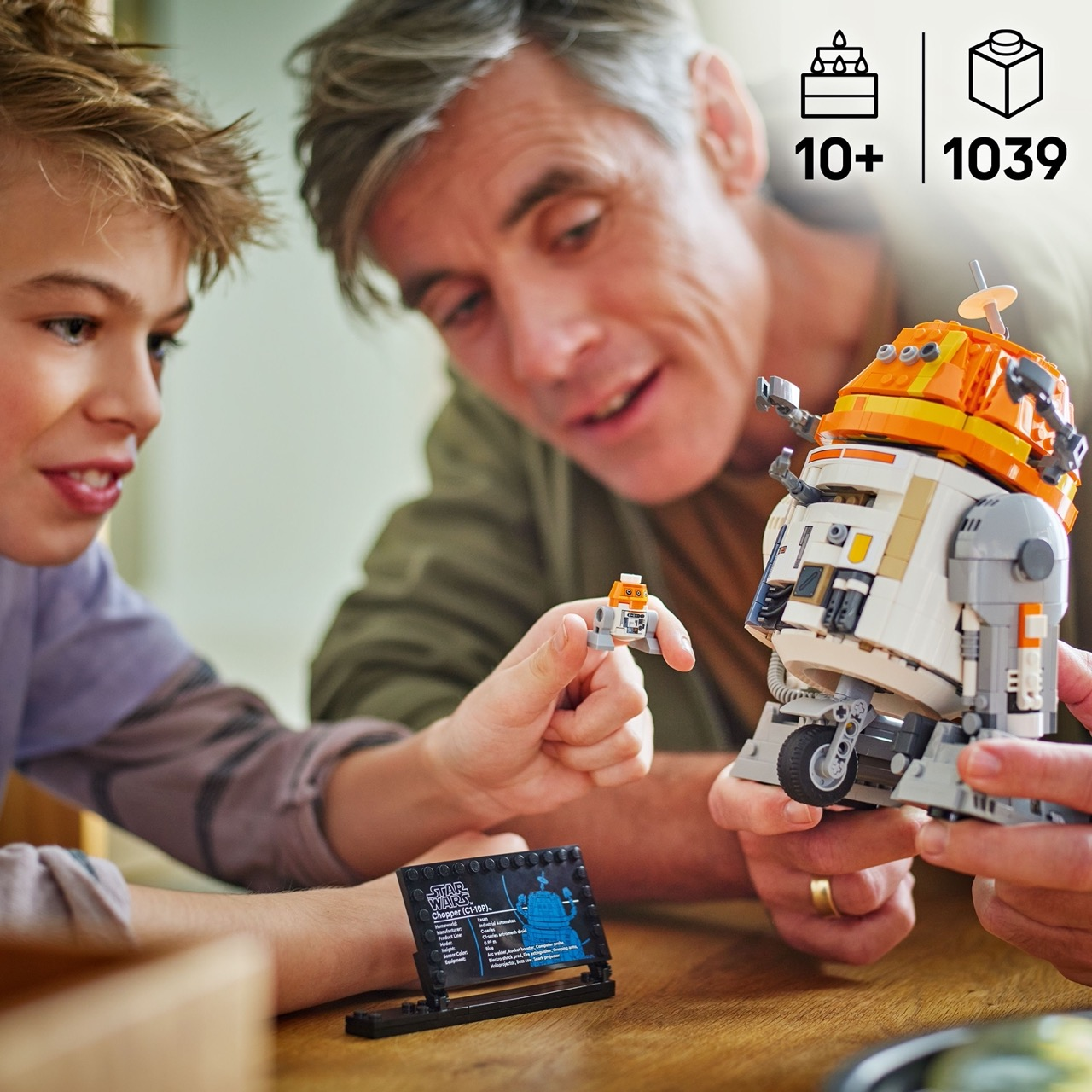 Un padre y su hijo construyen un robot Lego. El robot es blanco y naranja. El fondo incluye una pantalla Lego.