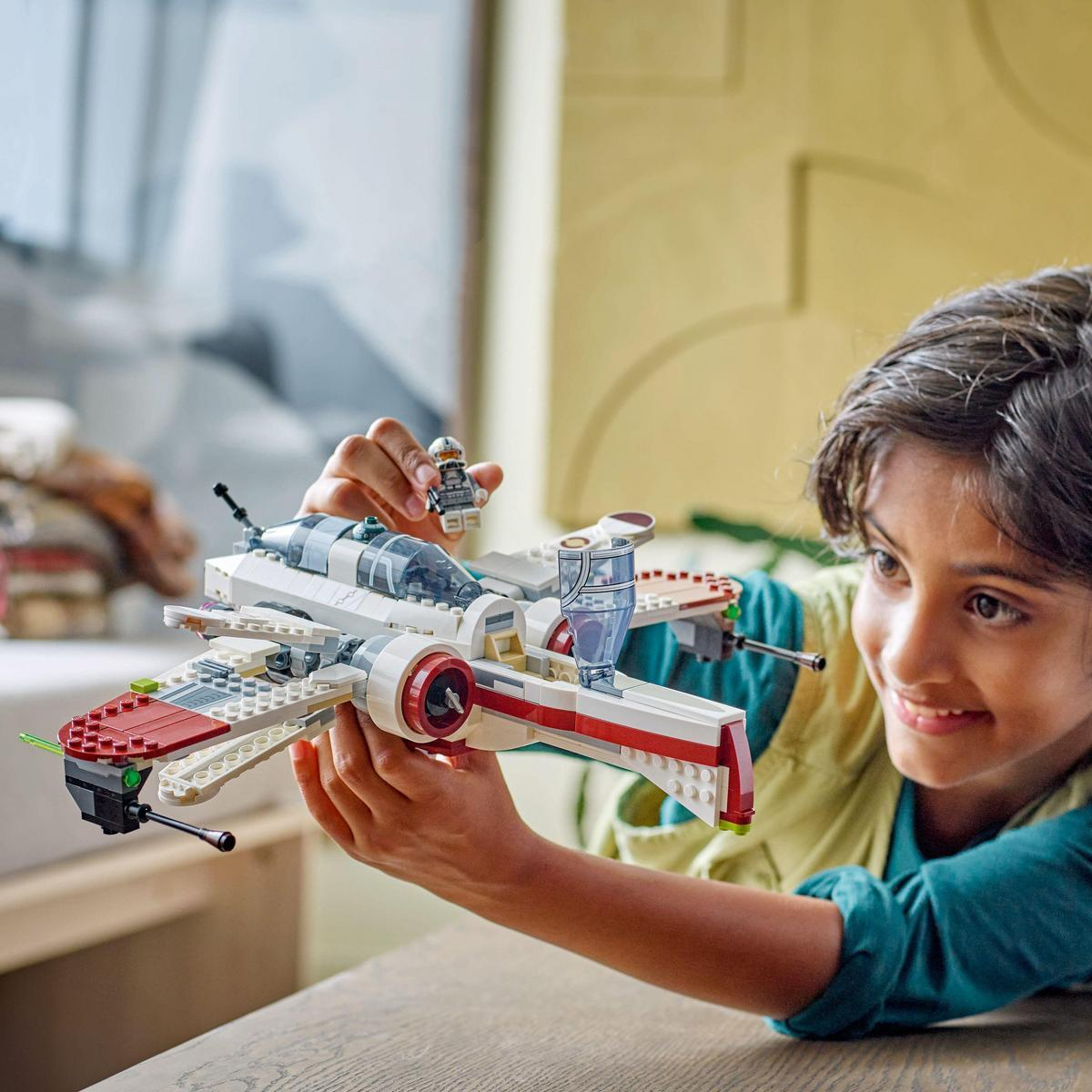 Dziecko trzyma myśliwiec LEGO X-wing. Myśliwiec jest biało-czerwony, z figurką pilota w środku.
