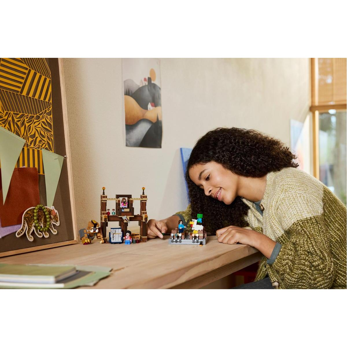 Dziewczyna uśmiecha się do modelu Lego. Przedstawia budynek z figurkami i małym mostem. Scena rozgrywa się na drewnianym stole.
