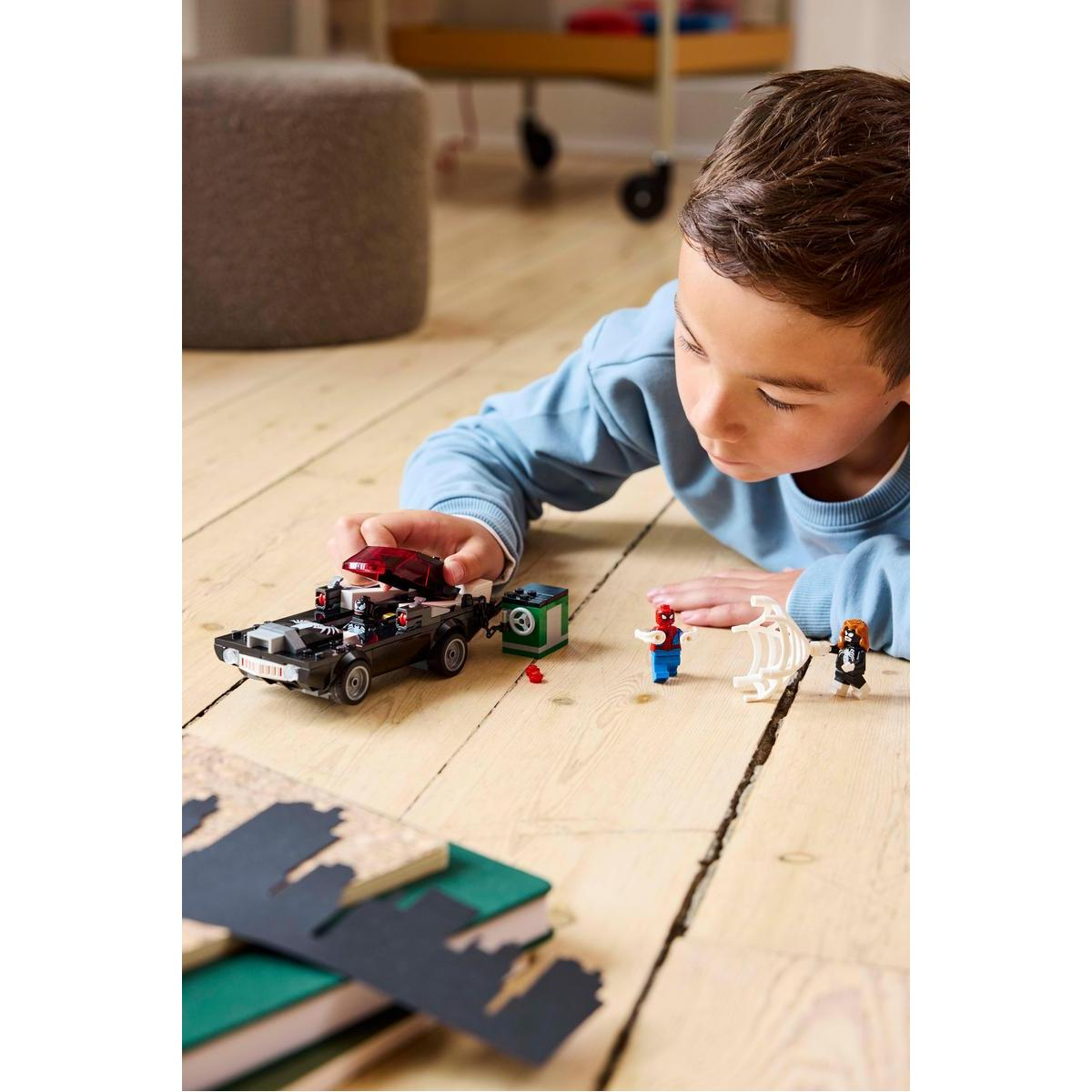 Chłopiec bawi się samochodem policyjnym Lego, Spider-Manem i innymi figurkami Lego na drewnianej podłodze.