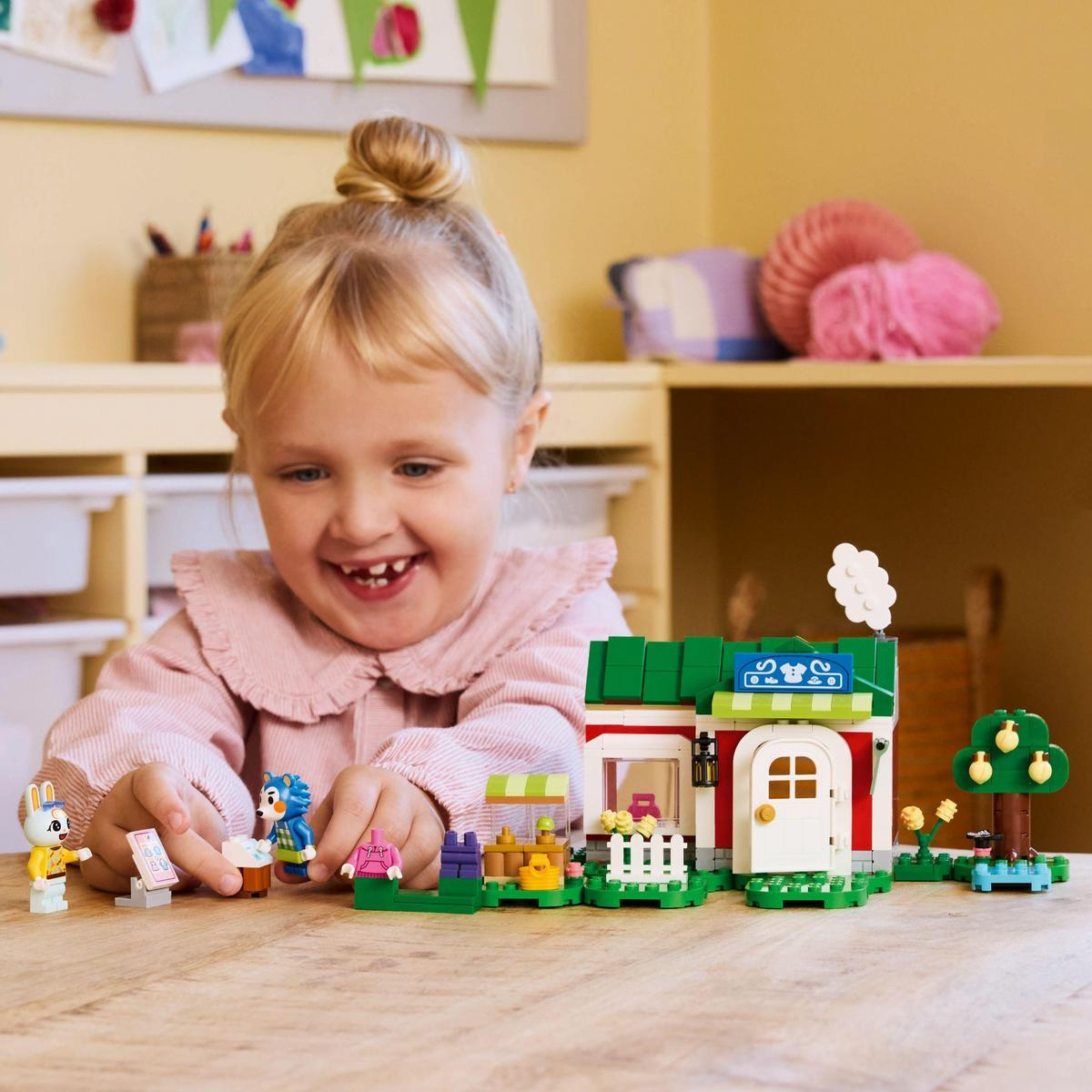 Uśmiechnięta dziewczynka bawi się zestawem Lego. Na stole jest sklep Lego z postaciami.