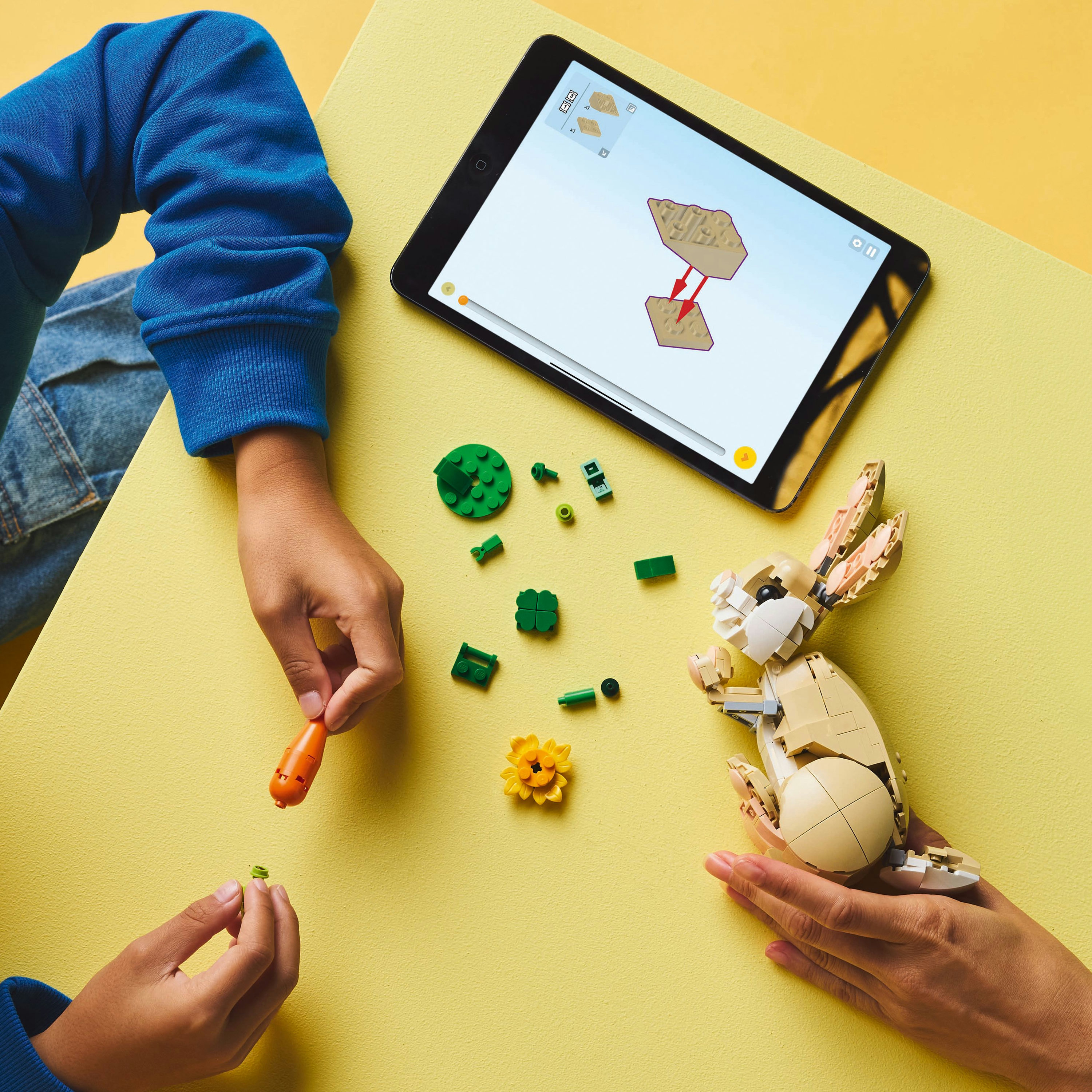 Osoba buduje królika Lego, z marchewką i kwiatkiem. W pobliżu tablet z instrukcjami.
