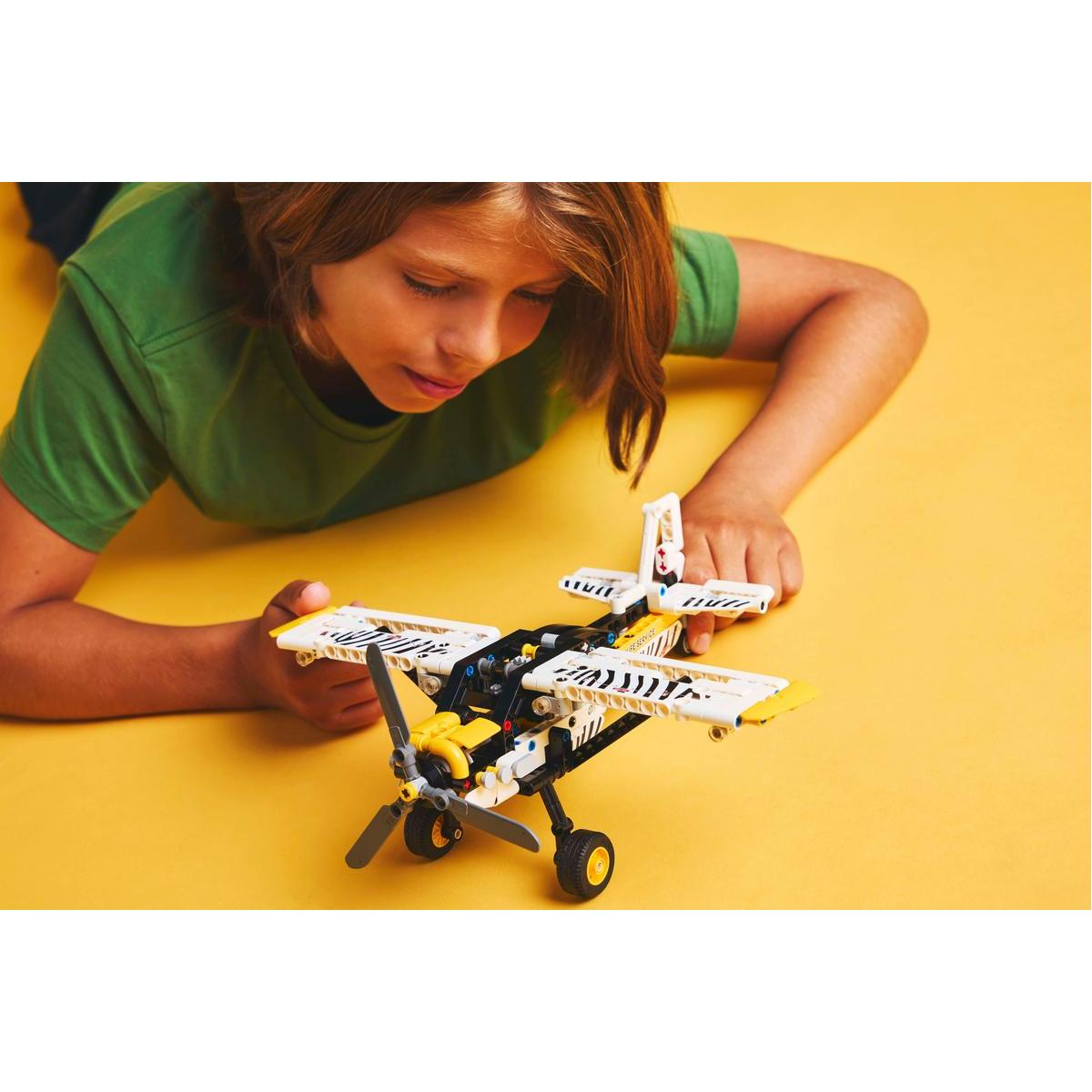 Dziecko patrzy na samolot Lego. Samolot jest biało-żółty z paskami zebry na żółtym tle.