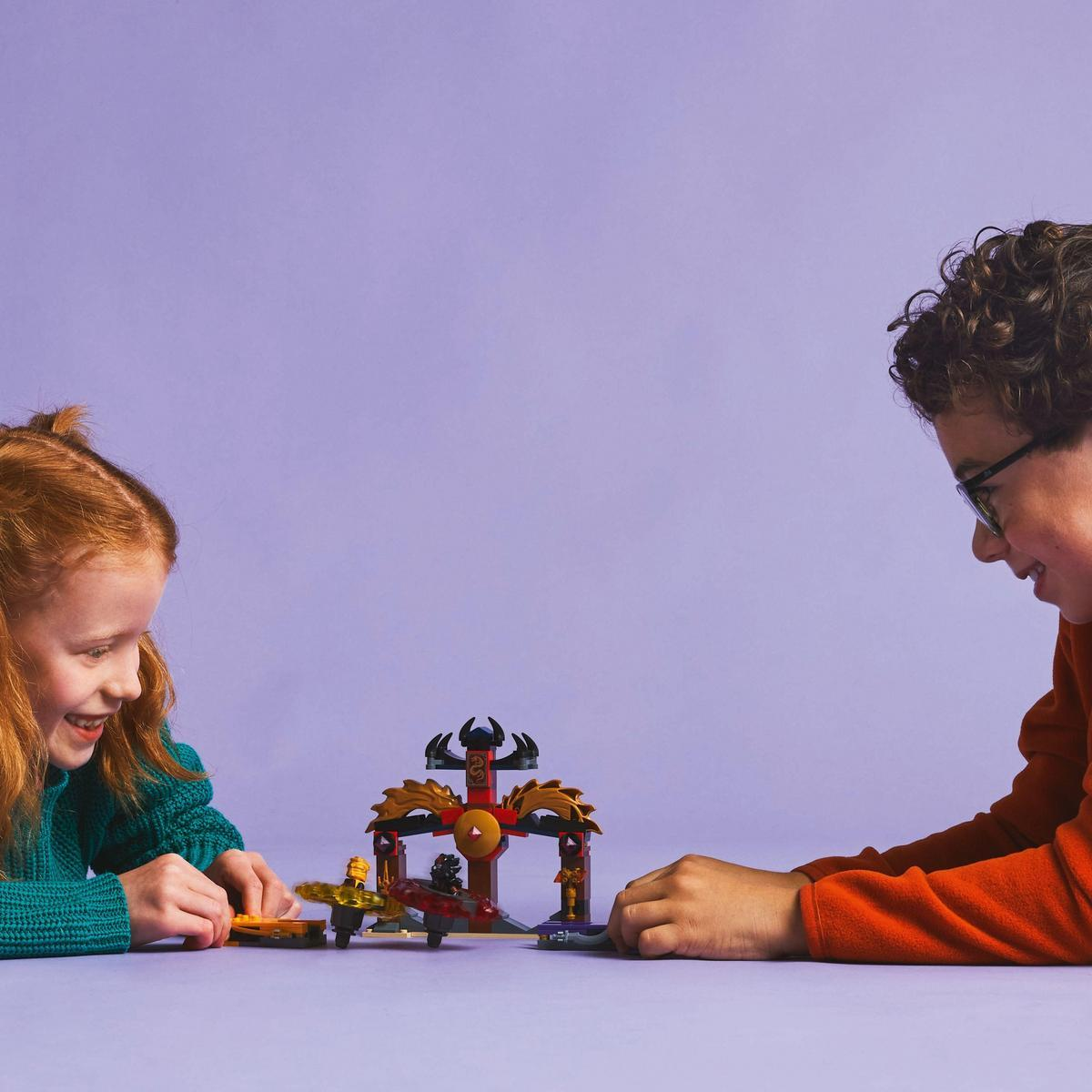 Dos niños jugando con un set de Lego. El set es una arena de peonzas doradas sobre fondo morado.