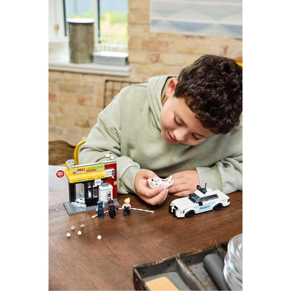 Chłopiec bawi się klockami Lego. Jest sklep i radiowóz. Są figurki mężczyzny, kobiety i dalmatyńczyka.