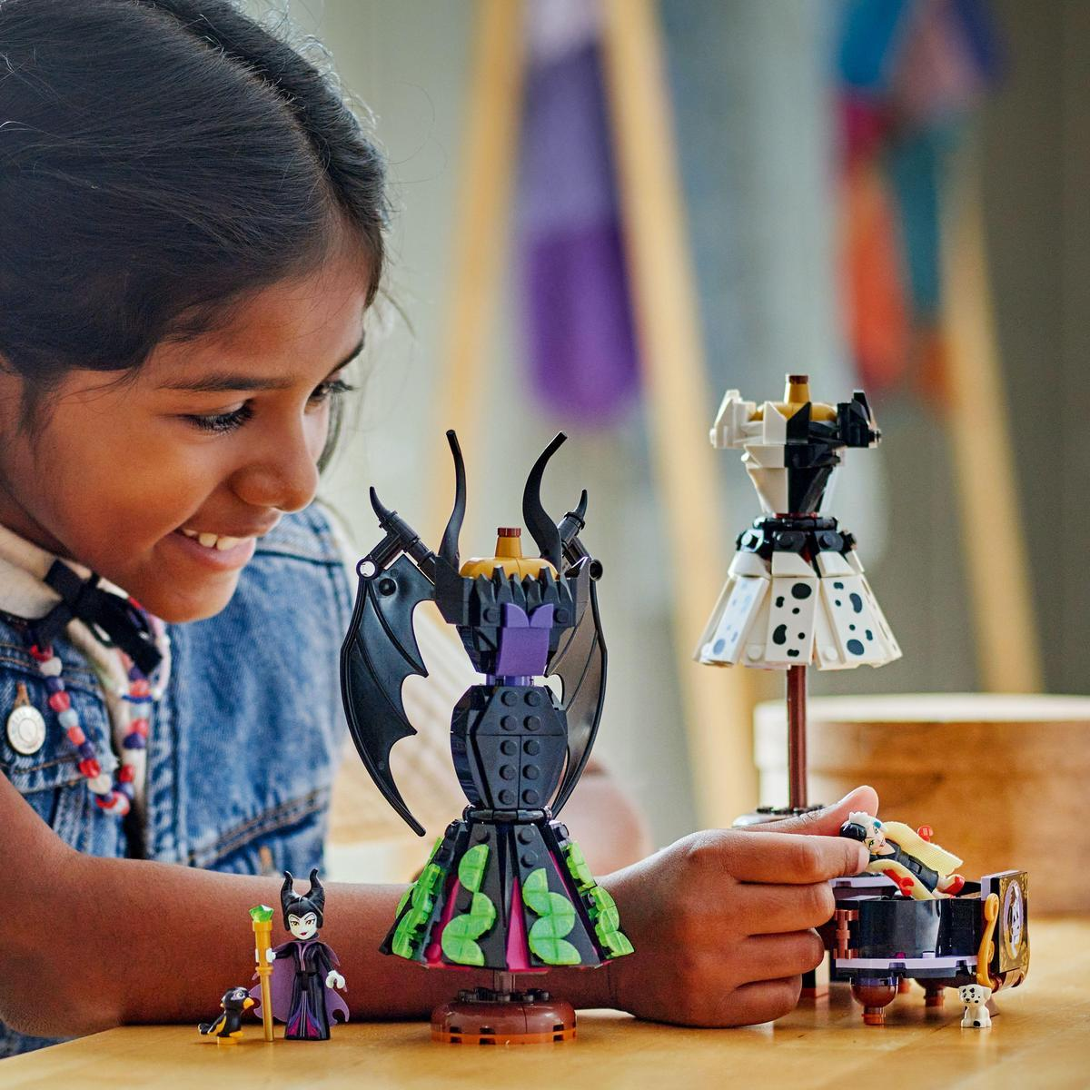 Dziewczynka bawi się zestawami Lego. Są dwie formy sukienek i fortepian. Obecna jest również figurka Maleficent.