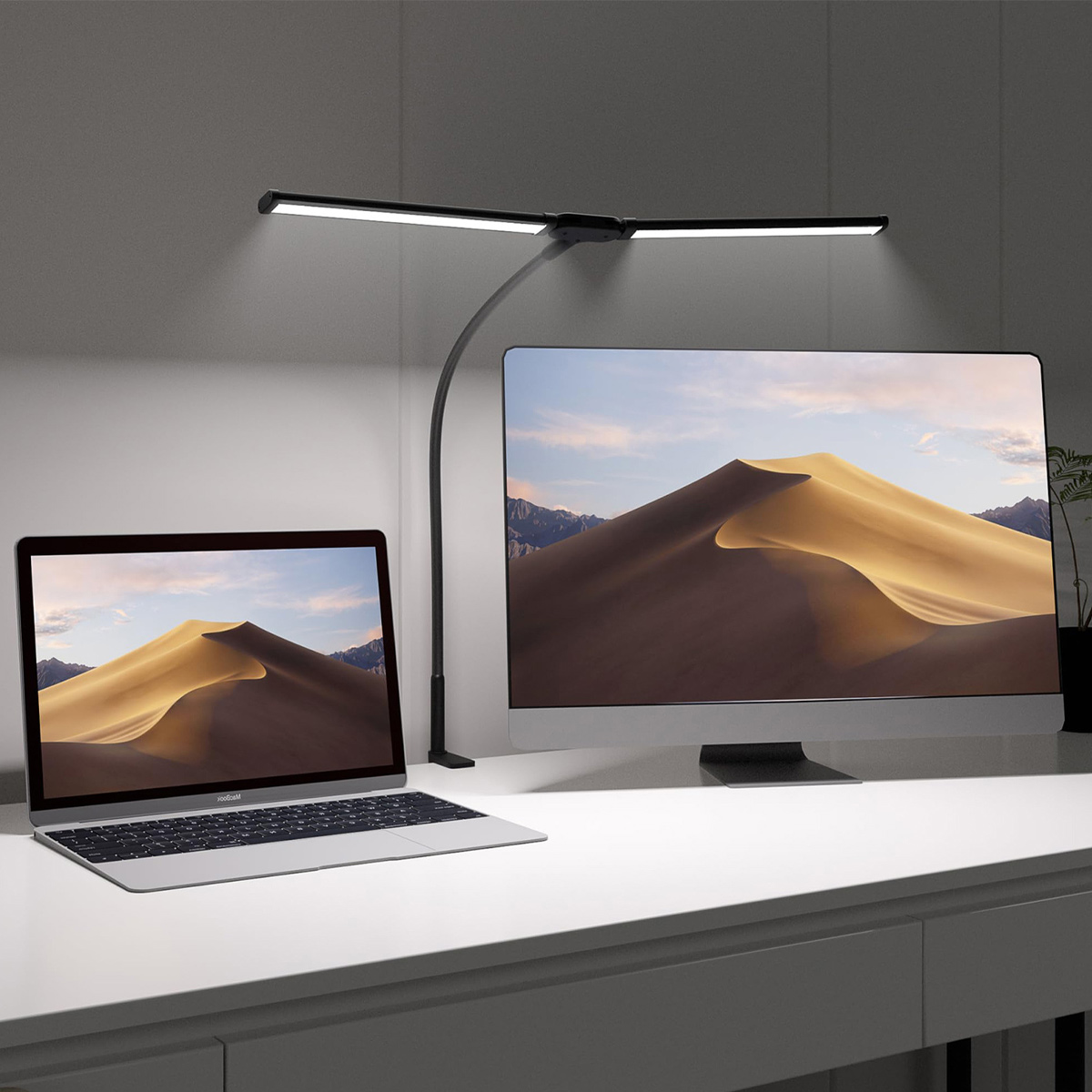 Uno schermo del computer, un laptop e una lampada da scrivania nera con due pannelli luminosi su una scrivania bianca.