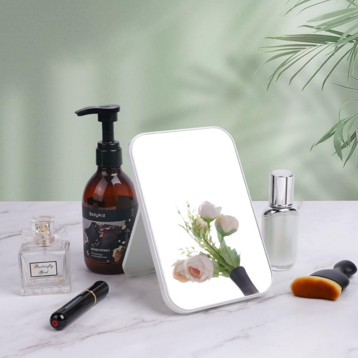 Spiegel, Parfümflaschen, Lotion und Make-up-Pinsel stehen auf Marmor. Blumen im Spiegel.