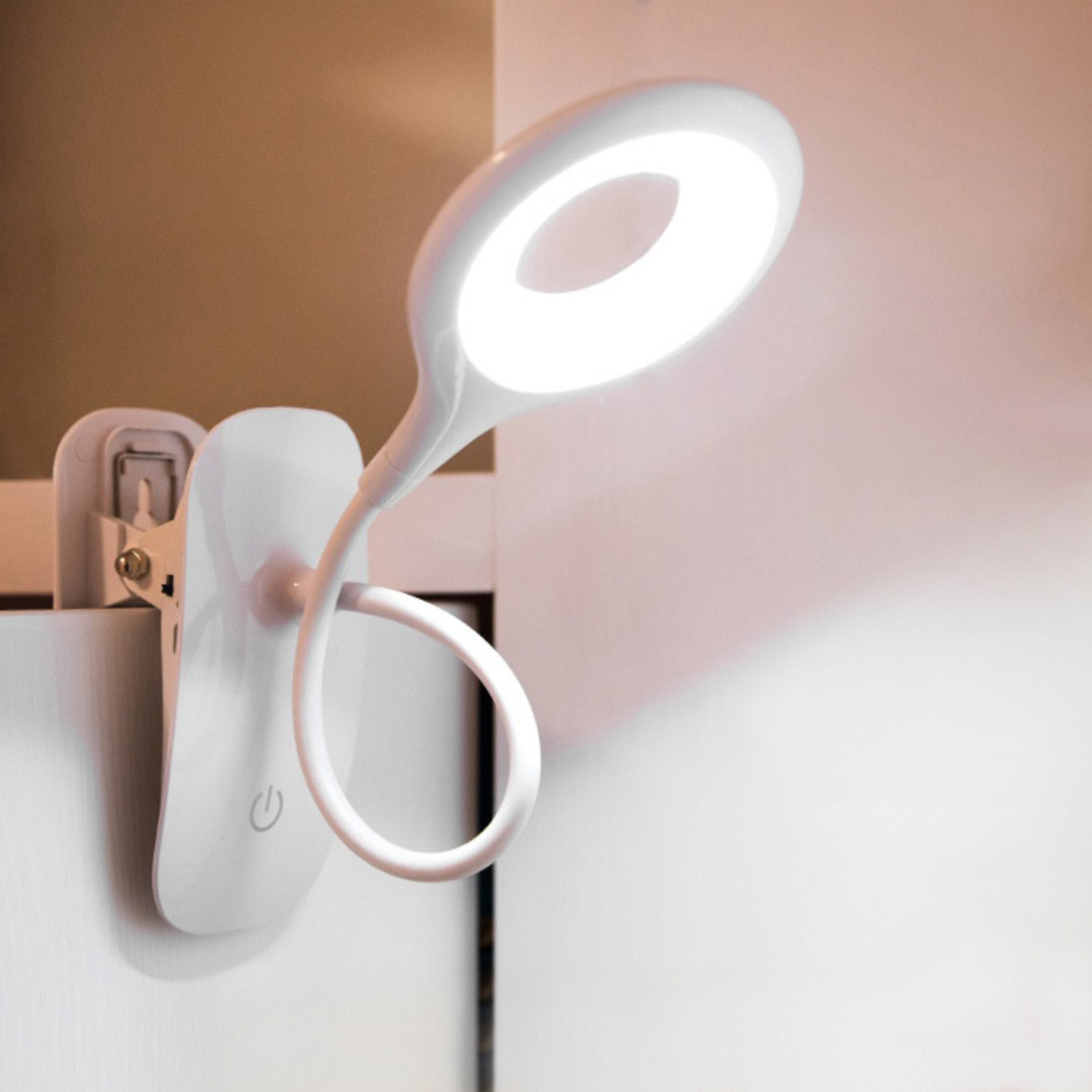Eine weiße Lampe mit kreisförmigem Licht, das auf eine weiße Wand scheint. Die Lampe hat einen Clip.