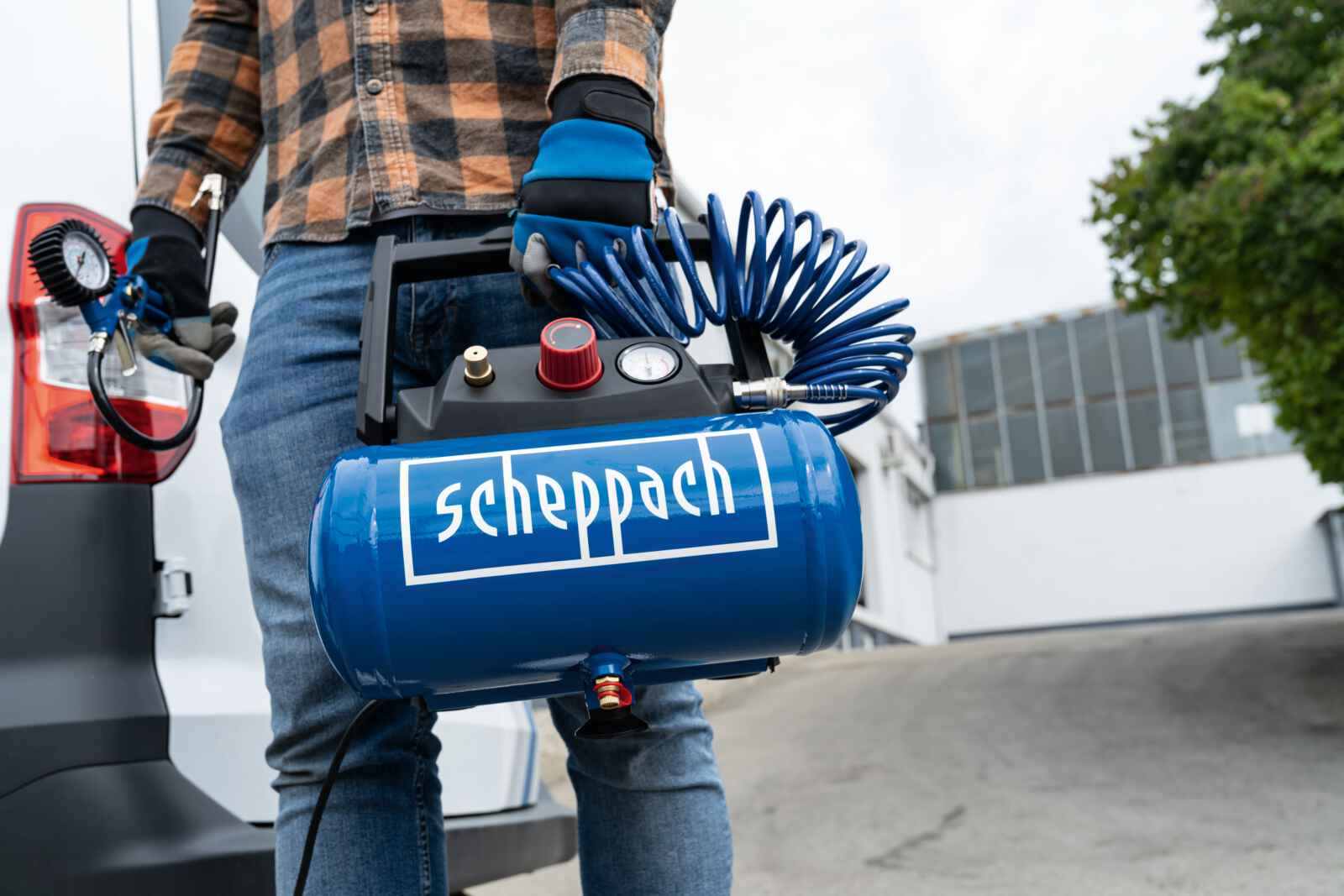 Een persoon die een blauw-zwarte luchtcompressor vasthoudt naast een witte bestelwagen.