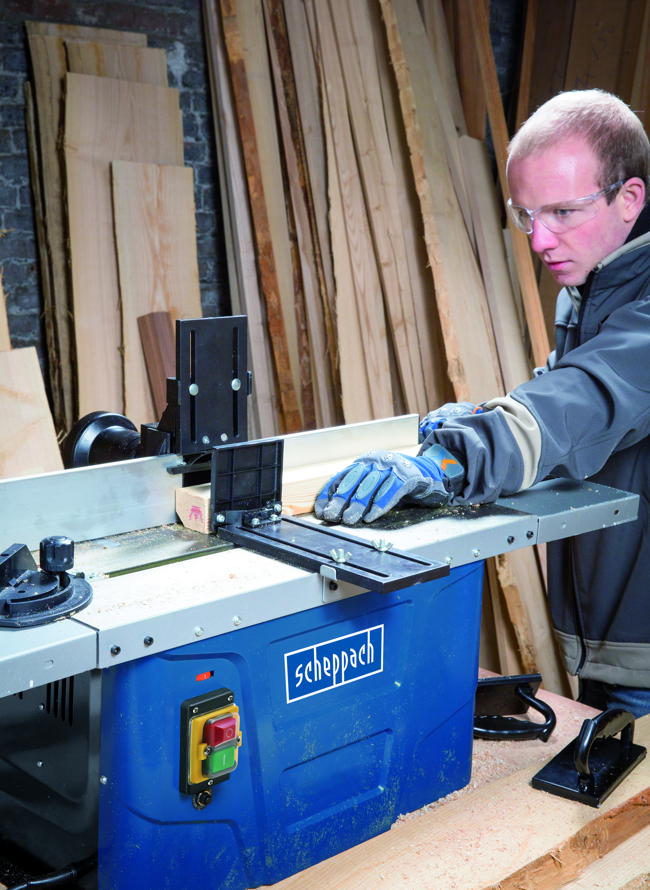 Un uomo che lavora con una macchina per la modellazione del legno, che utilizza occhiali di sicurezza, modellando un pezzo di legno.