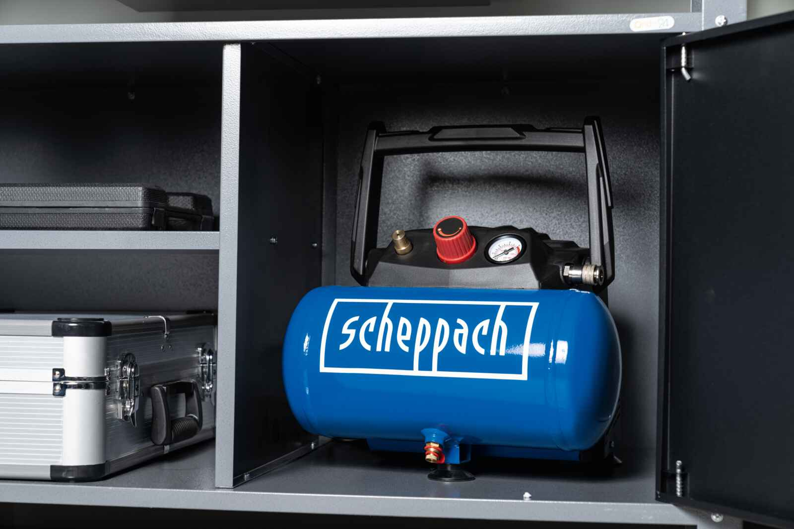 Een blauwe luchtcompressor staat in een kast. De compressor heeft een zwarte bovenkant en rode meters.