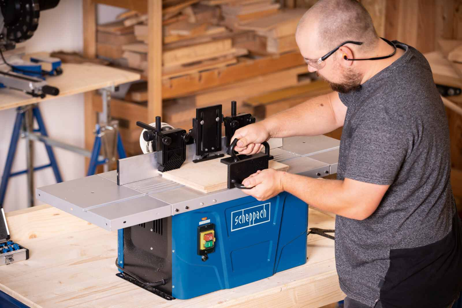 Un uomo che utilizza una macchina per la lavorazione del legno Scheppach blu, modellando un pezzo di legno su un banco da lavoro.