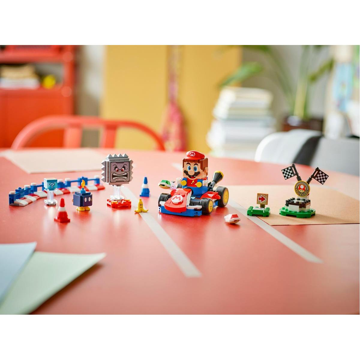 Set Lego Mario Kart su un tavolo rosso. Personaggio di Mario in un kart, con ostacoli come blocchi e un traguardo.