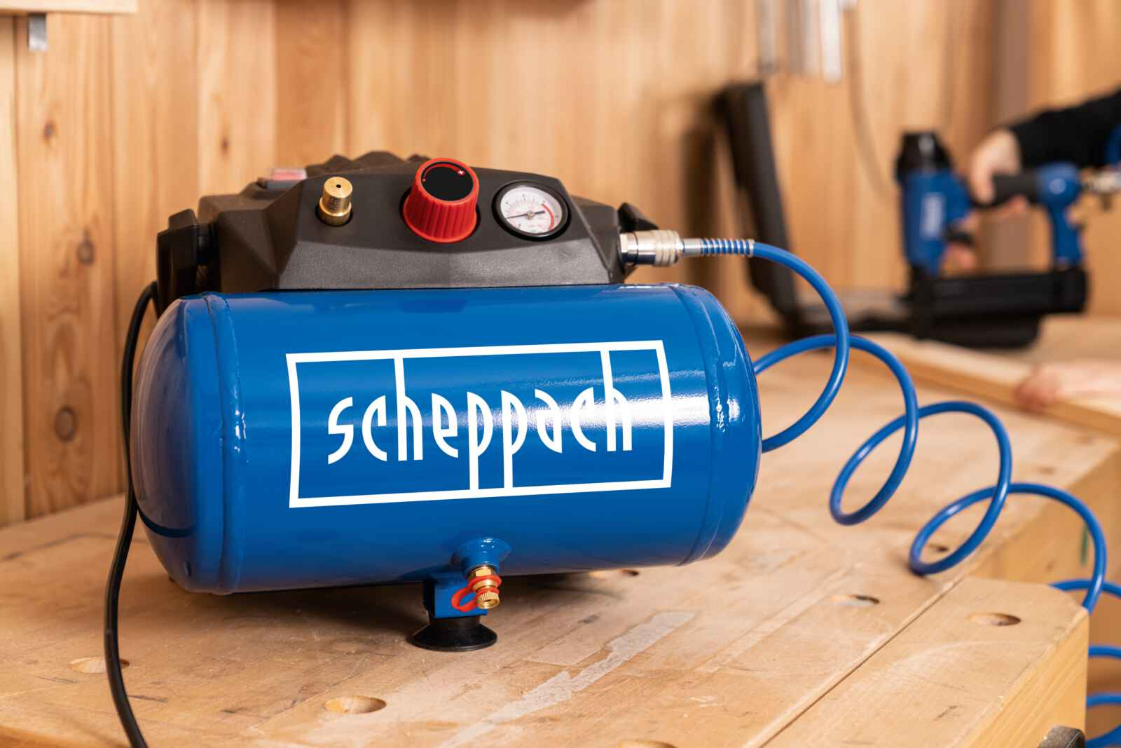 Een blauwe luchtcompressor op een houten tafel. Hij heeft een zwarte bovenkant met meters en een wit logo.