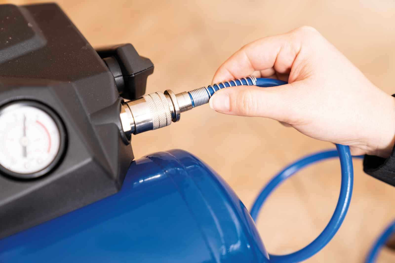 Een hand verbindt een blauwe slang met een compressor. De compressor is blauw en zwart.
