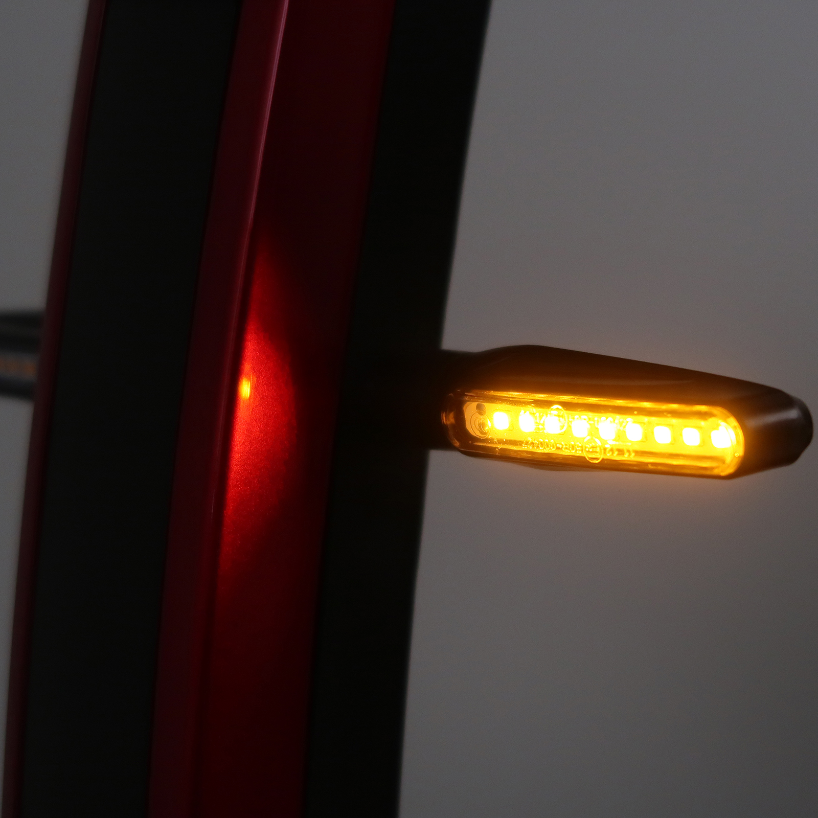 Der rechte Blinker eines roten Mobilitätsrollers, gelb beleuchtet.