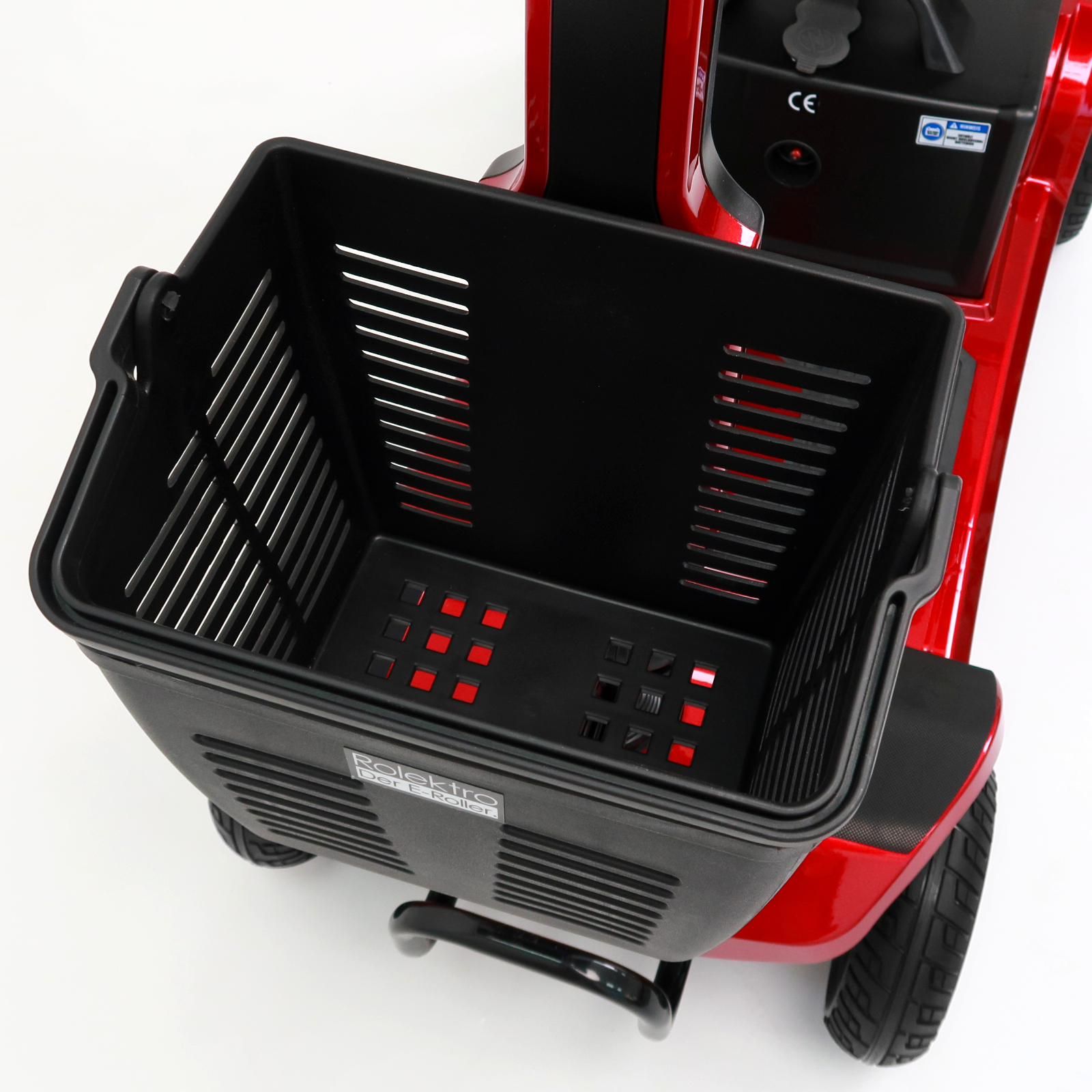 Ein roter Mobilitätsroller mit schwarzem Korb vorne. Der Roller hat schwarze Reifen und steht auf weißem Untergrund.