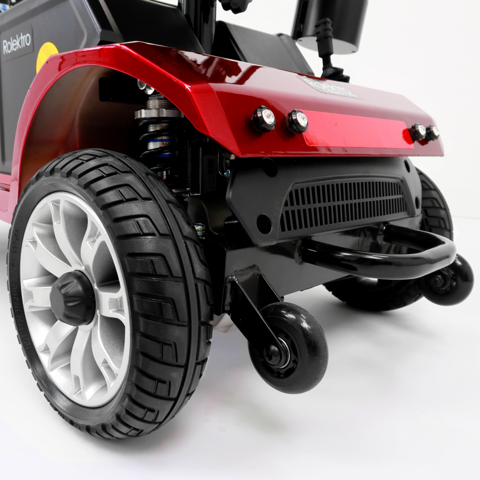 Roter Mobilitätsroller auf weißem Hintergrund. Merkmale sind große Vorderräder, schwarze Reifen und eine schwarze Stoßstange.