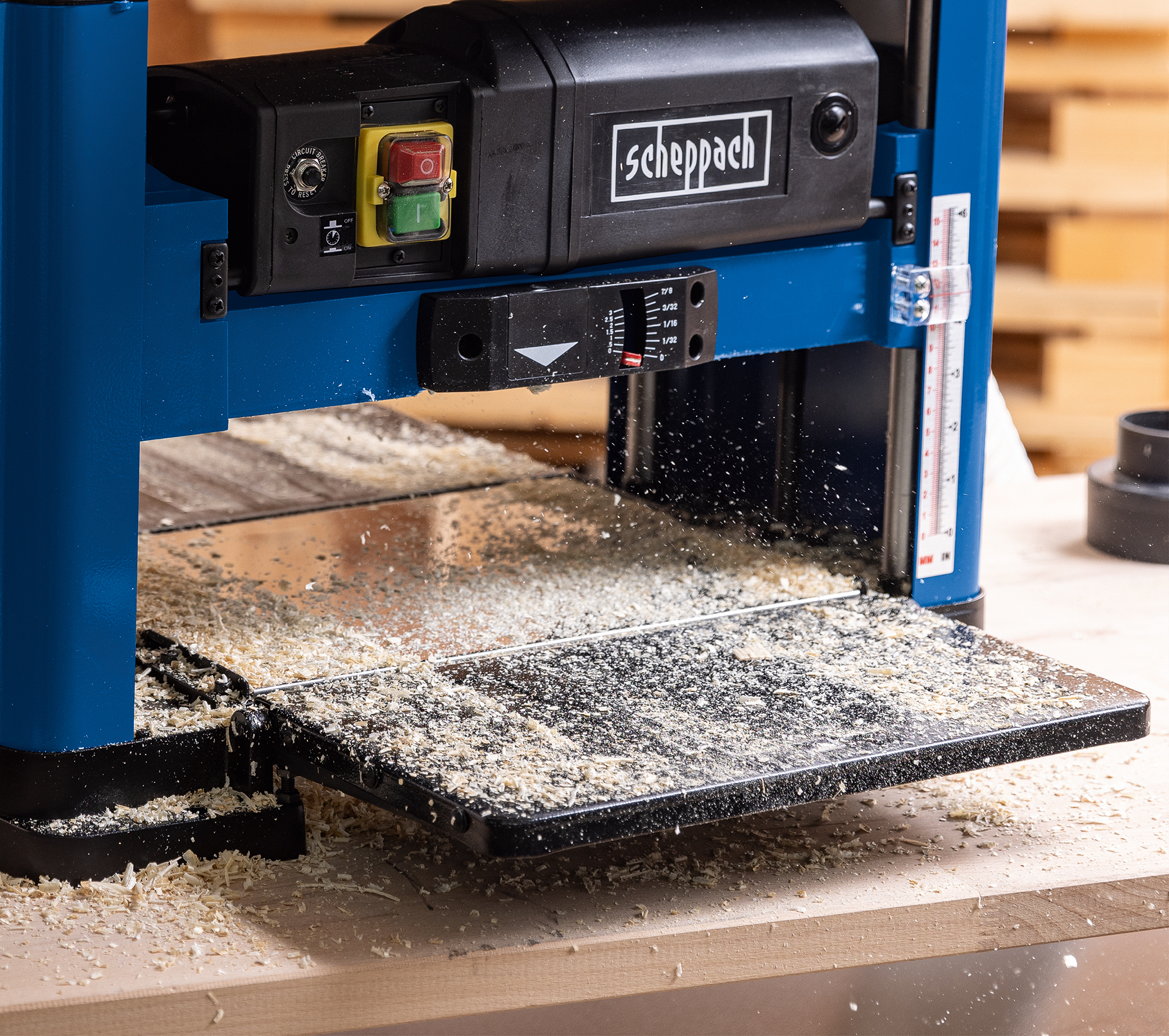 Een houtschaafmachine met houtsnippers. Hout wordt geschaafd, het Scheppach logo is zichtbaar.