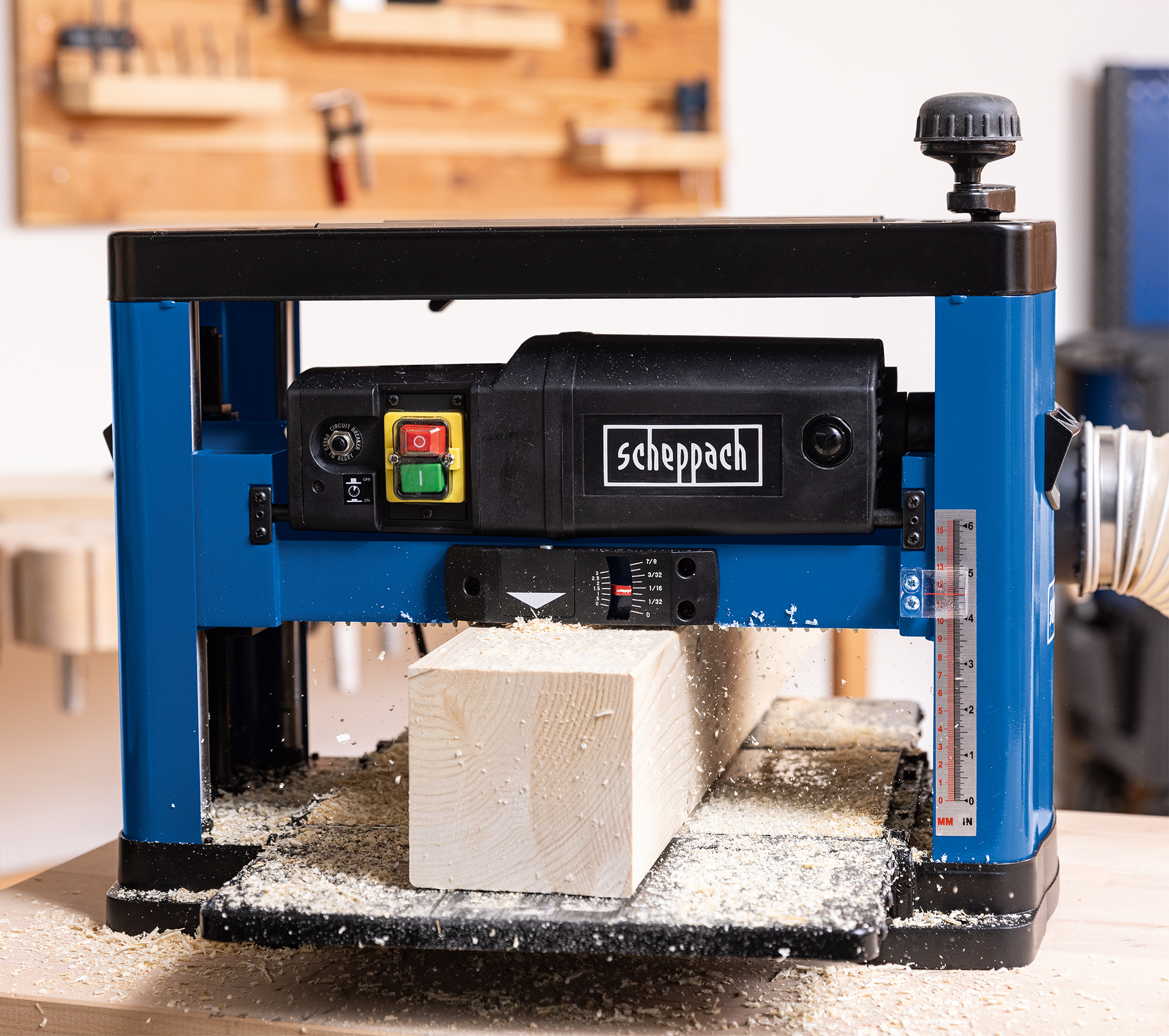 Een blauw-zwarte schaafmachine schaaft een houten balk. Zaagsel omringt de machine.
