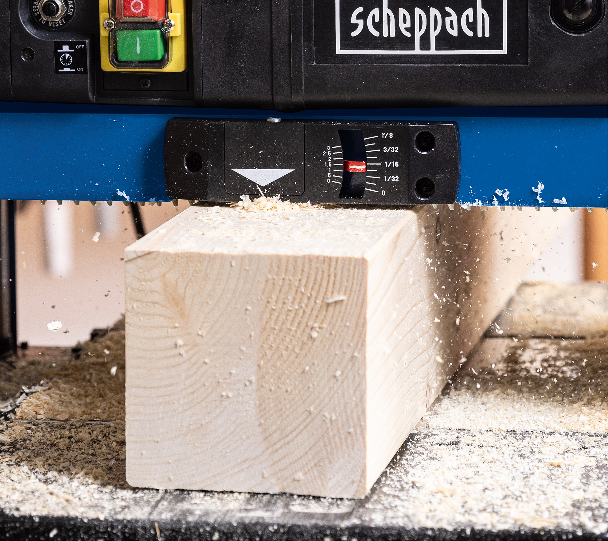 Een schaafmachine bewerkt een blok hout. Houtsnippers zijn zichtbaar. De machine is blauw en zwart.