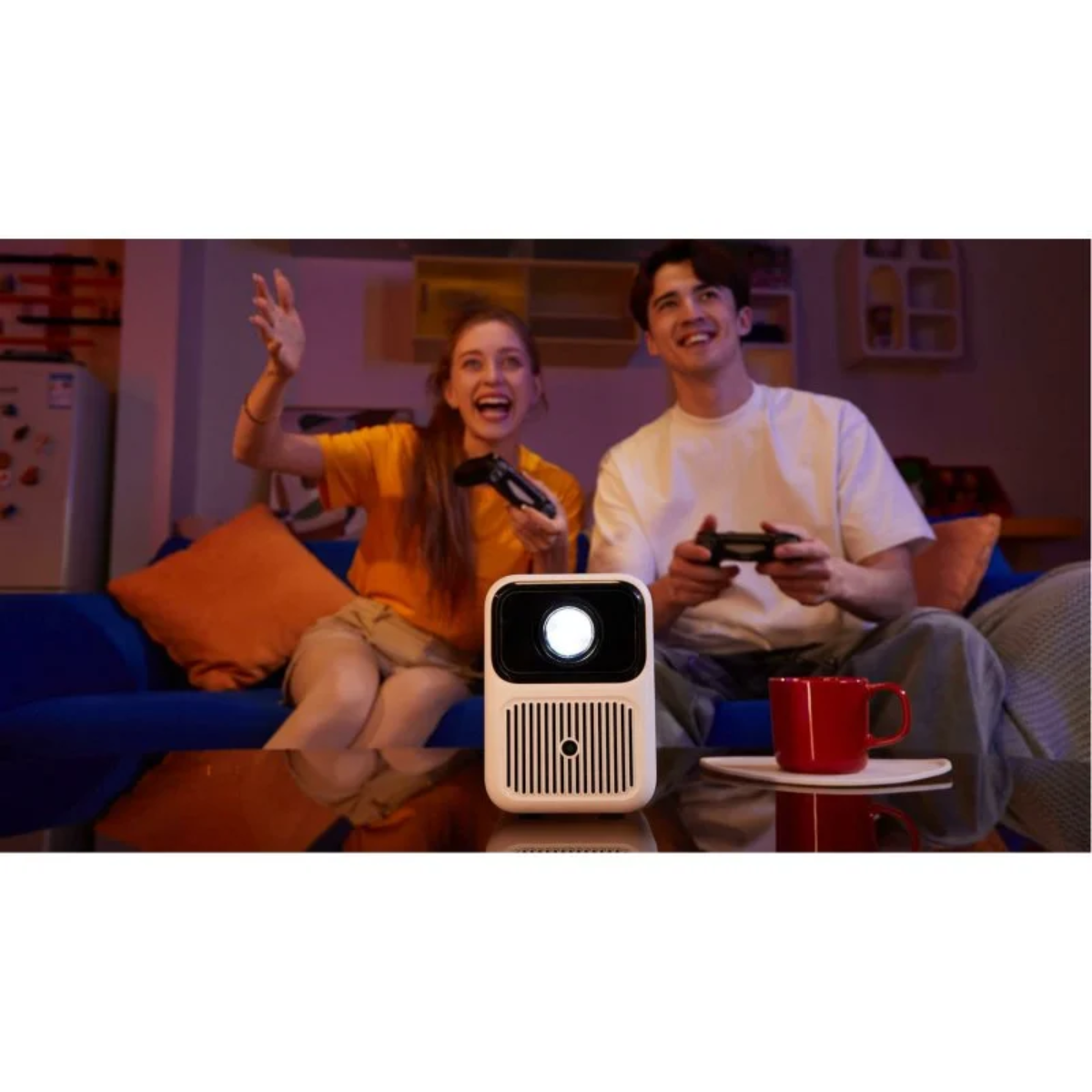 Una coppia gioca ai videogiochi, eccitata. Un proiettore bianco di fronte a loro. Tazza rossa a destra.