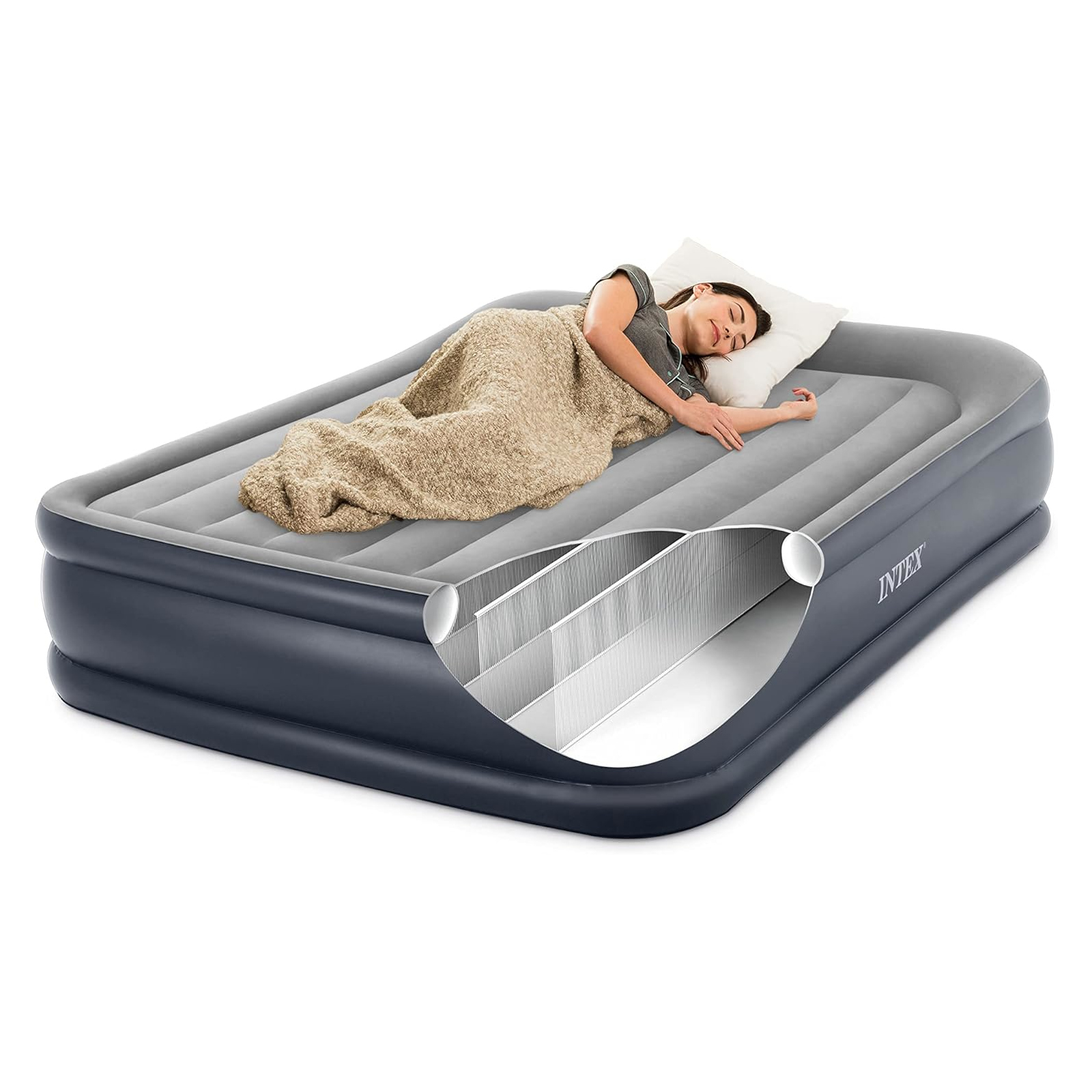 Una mujer durmiendo en una cama inflable, cubierta con una manta, la cabeza sobre una almohada. La cama es gris y negra.