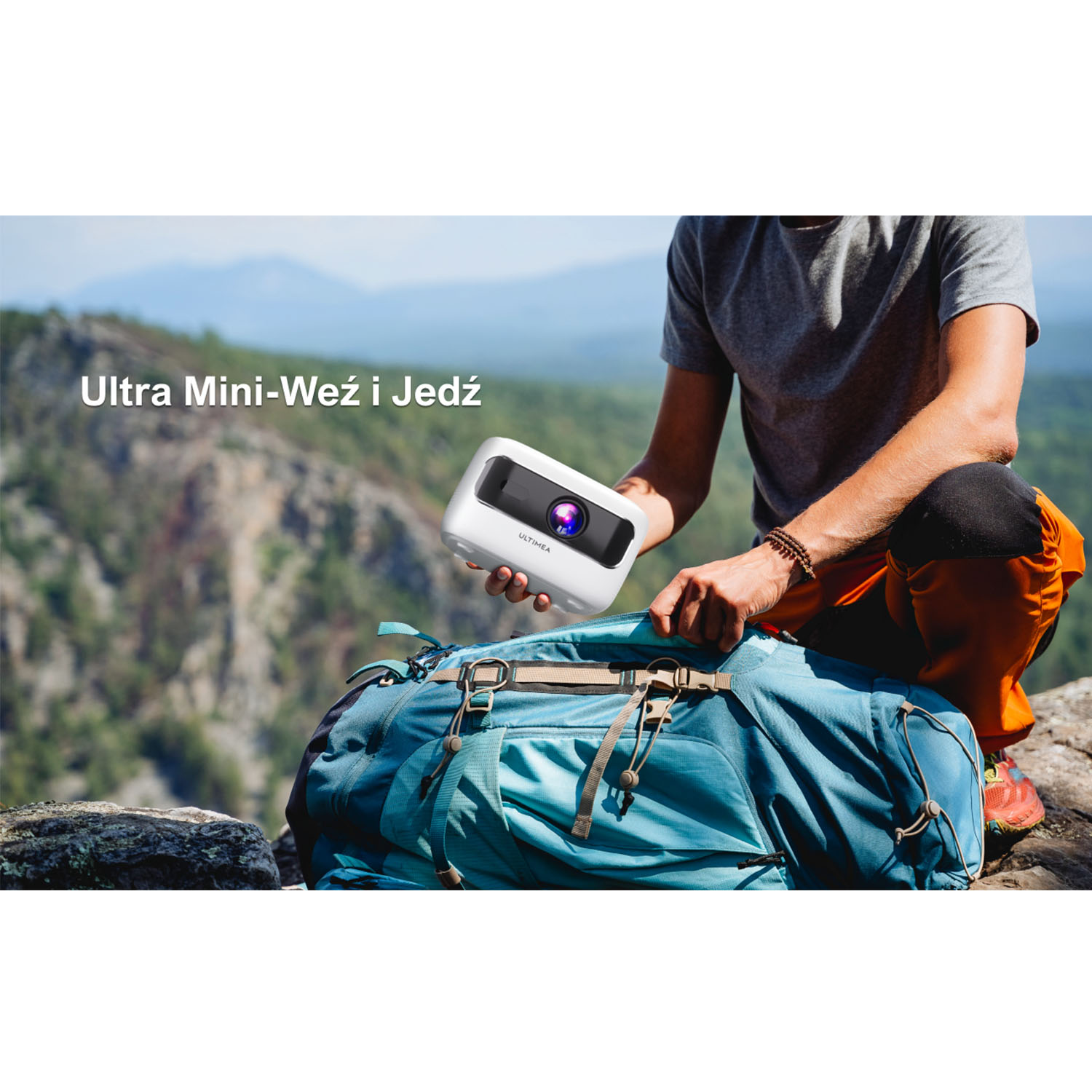 Osoba trzymająca biały projektor z widokiem na góry w tle i niebieski plecak. Tekst: Ultra Mini-Weż i Jedź.