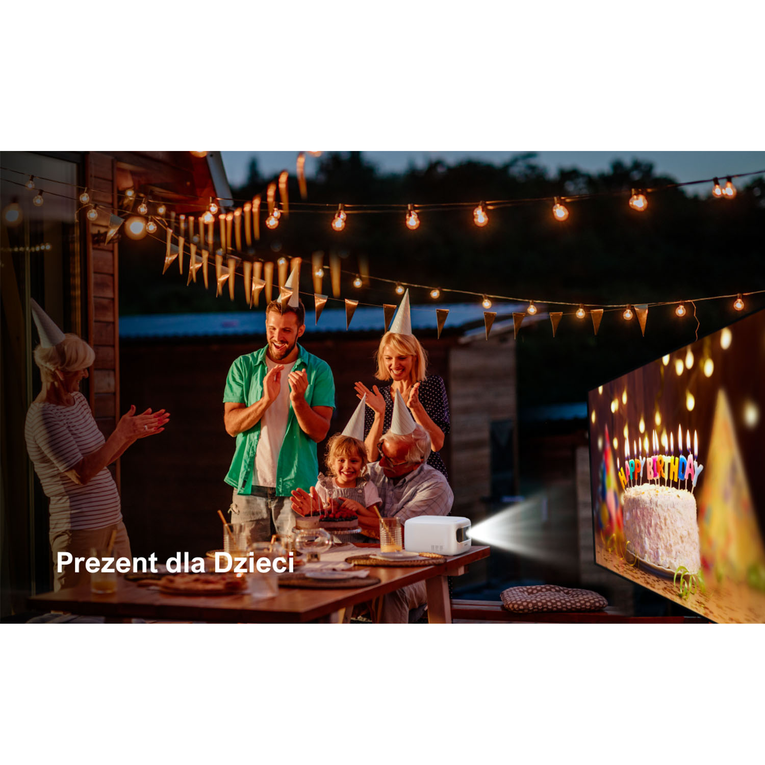 Rodzina świętująca urodziny na świeżym powietrzu, z tortem w tle. Tekst: Present dla Dzieci.
