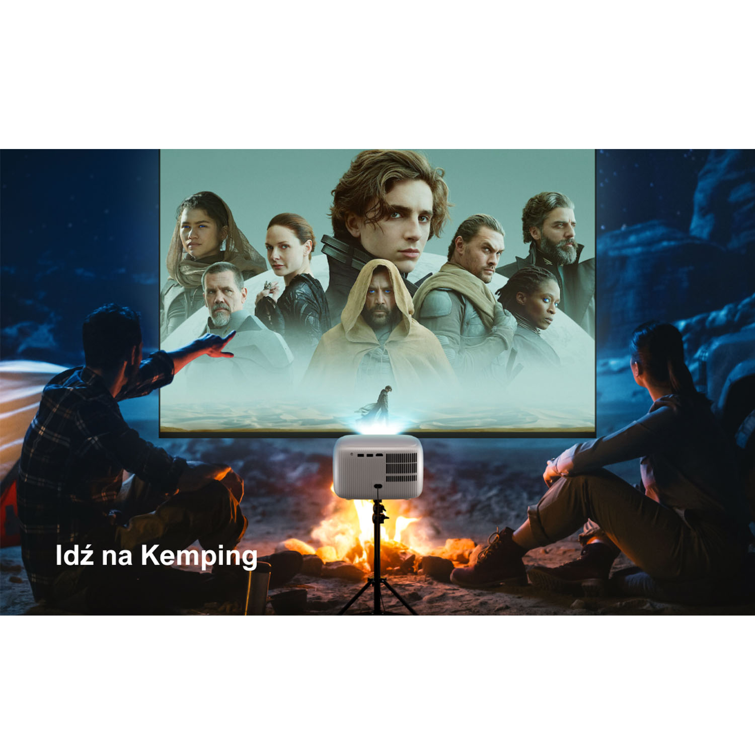 Ludzie oglądają film wyświetlany na ekranie. Projektor stoi na statywie. Z przodu jest ognisko.