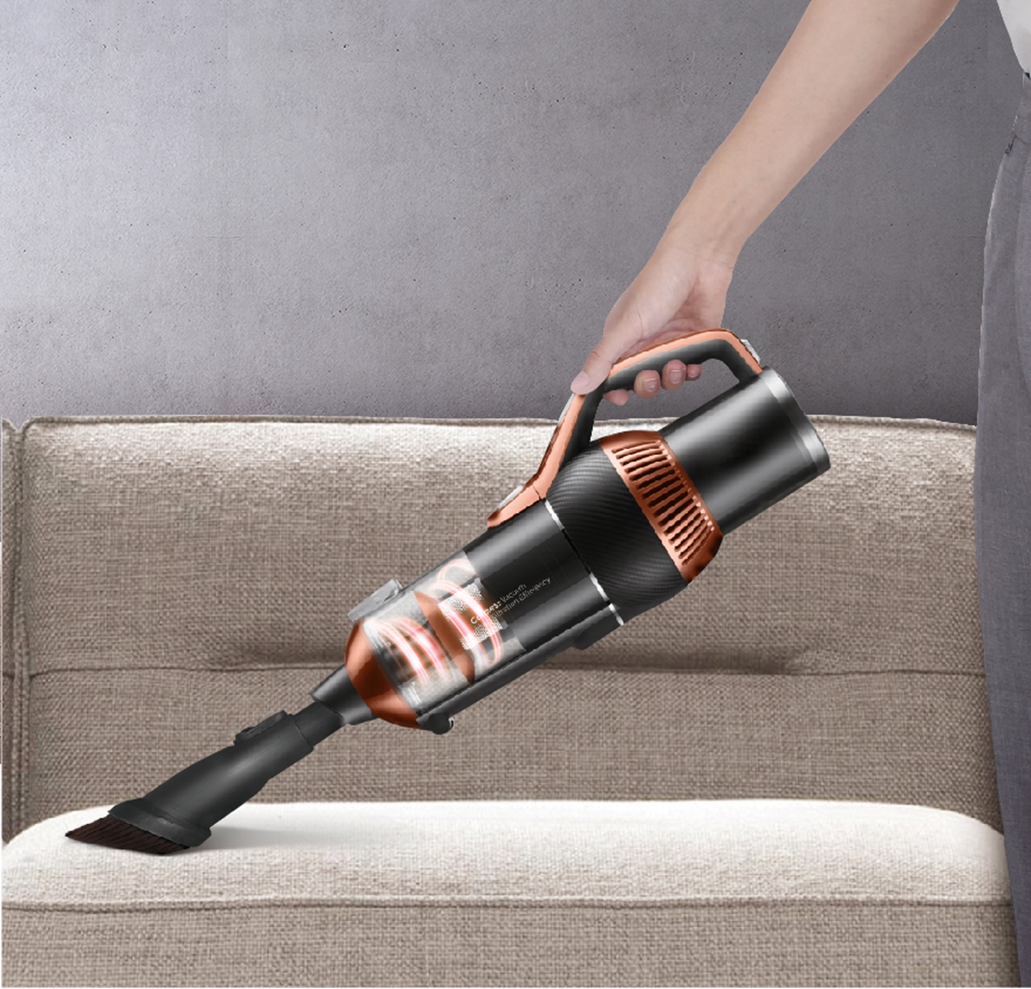 Eine Person saugt ein beiges Sofa mit einem Handstaubsauger. Der Staubsauger hat ein schwarz-kupferfarbenes Design.