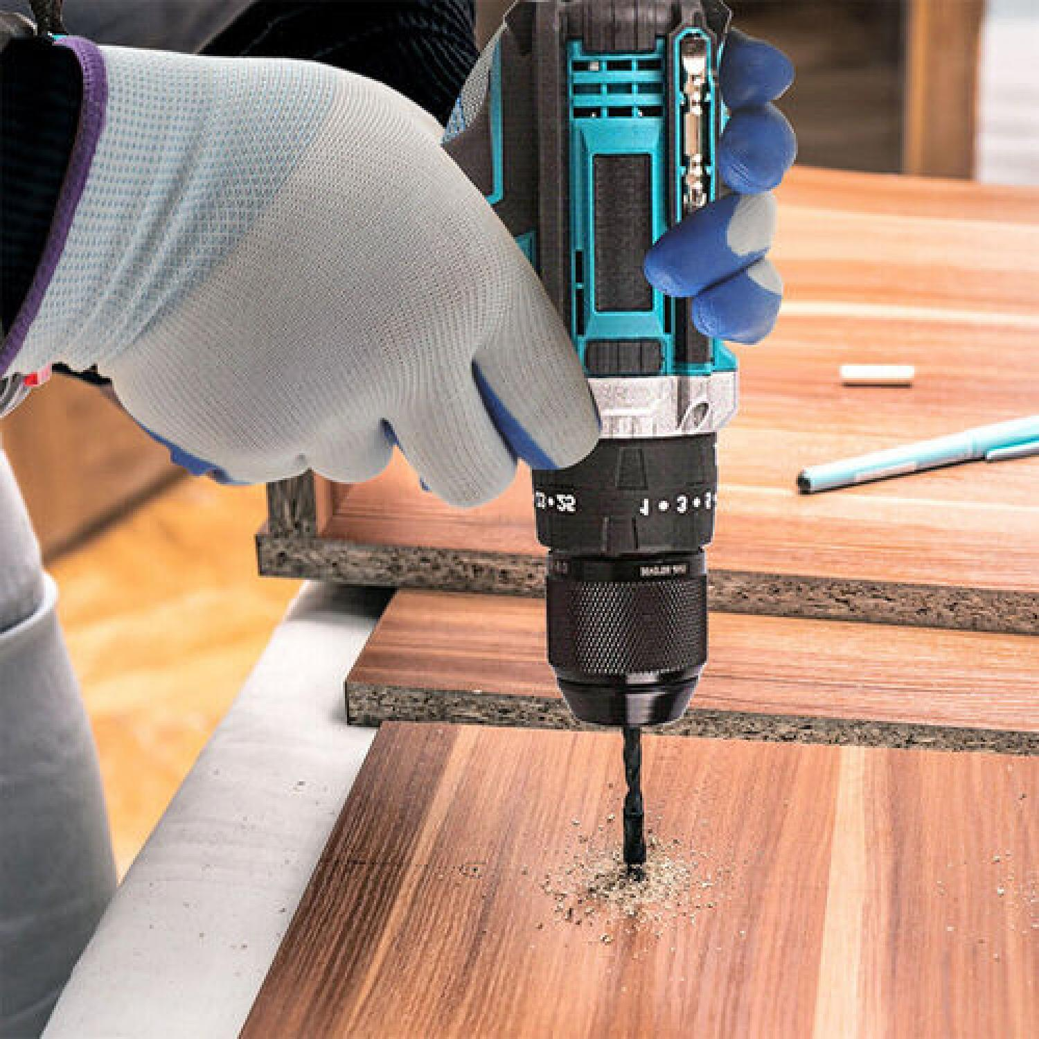 Eine Person mit Handschuhen verwendet eine türkisfarbene und schwarze Bohrmaschine, um in ein Holzstück zu bohren.
